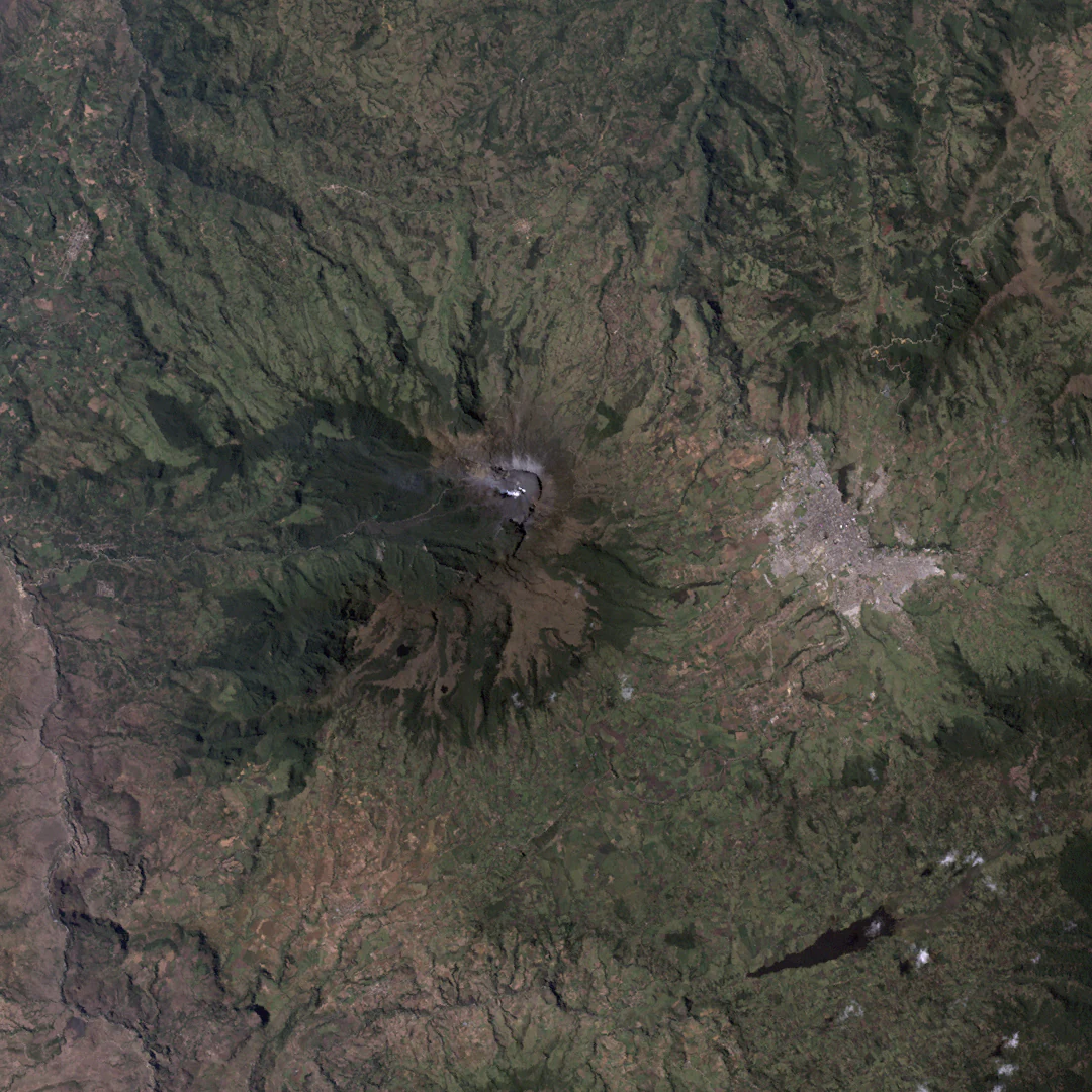 Satellite image showing Galeras Volcano with a volcanic crater, surrounding green terrain, and an urban settlement nearby