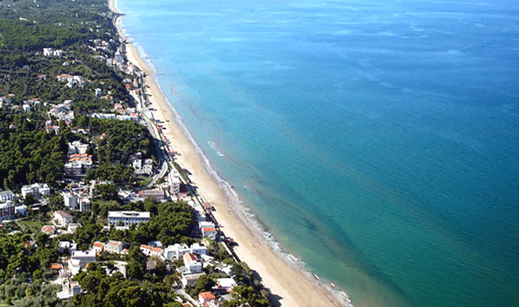 Aerial view of San Menaio beach, coastal town with white buildings, and turquoise sea extending to the horizon