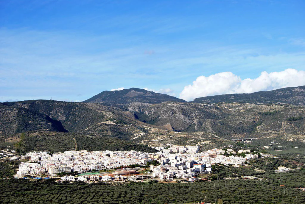 Panoramic view of Mattinata town with white buildings, set in a valley with forested hills and mountains under a blue sky