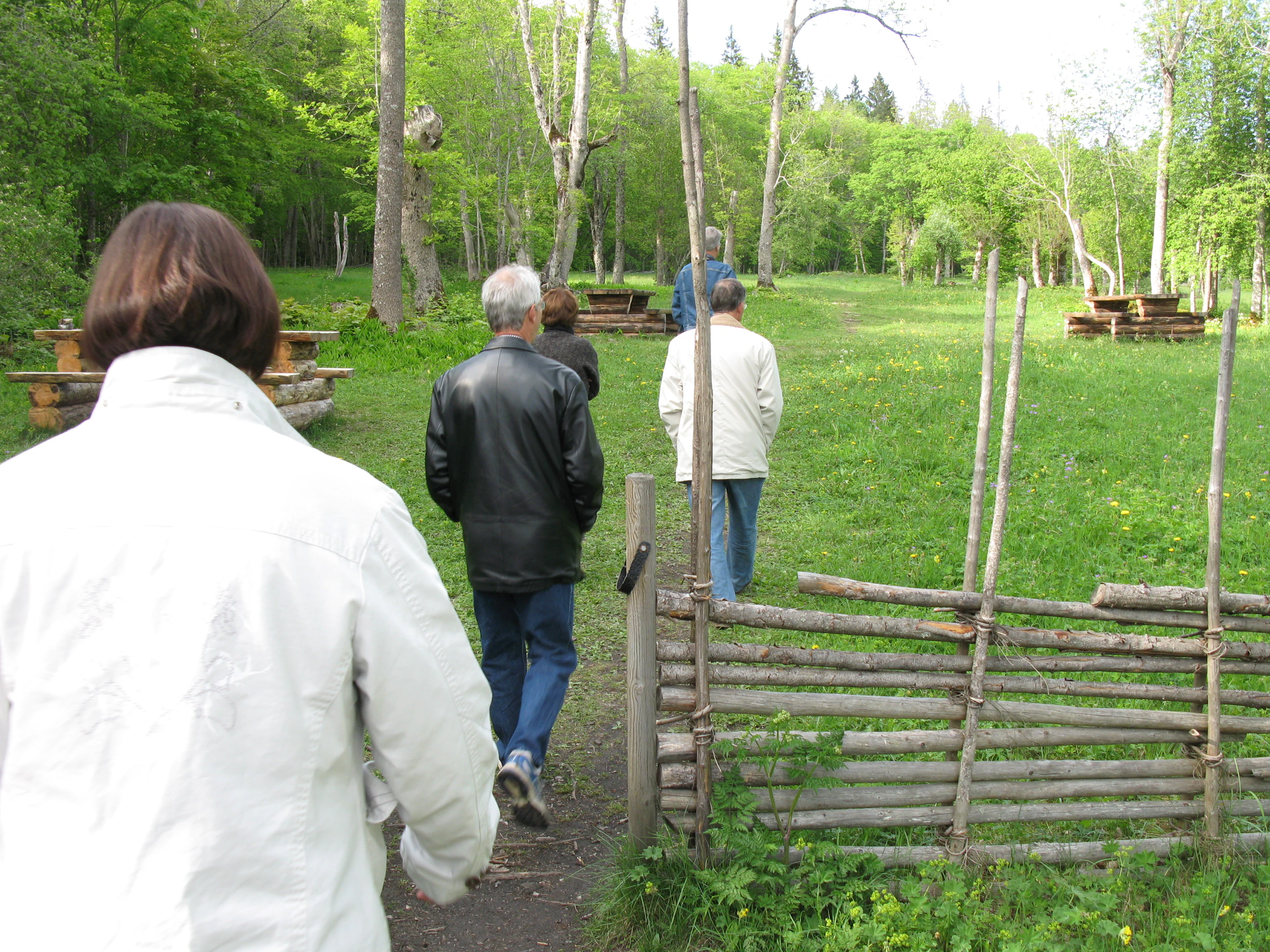 Group of people walking on a dirt path through a grassy area with wooden fences and trees