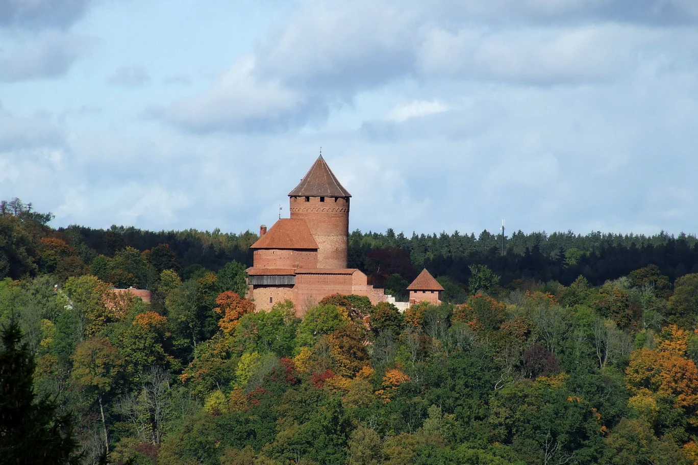 Red-brick castle with a tower situated on a hill amidst autumn foliage and a forested landscape