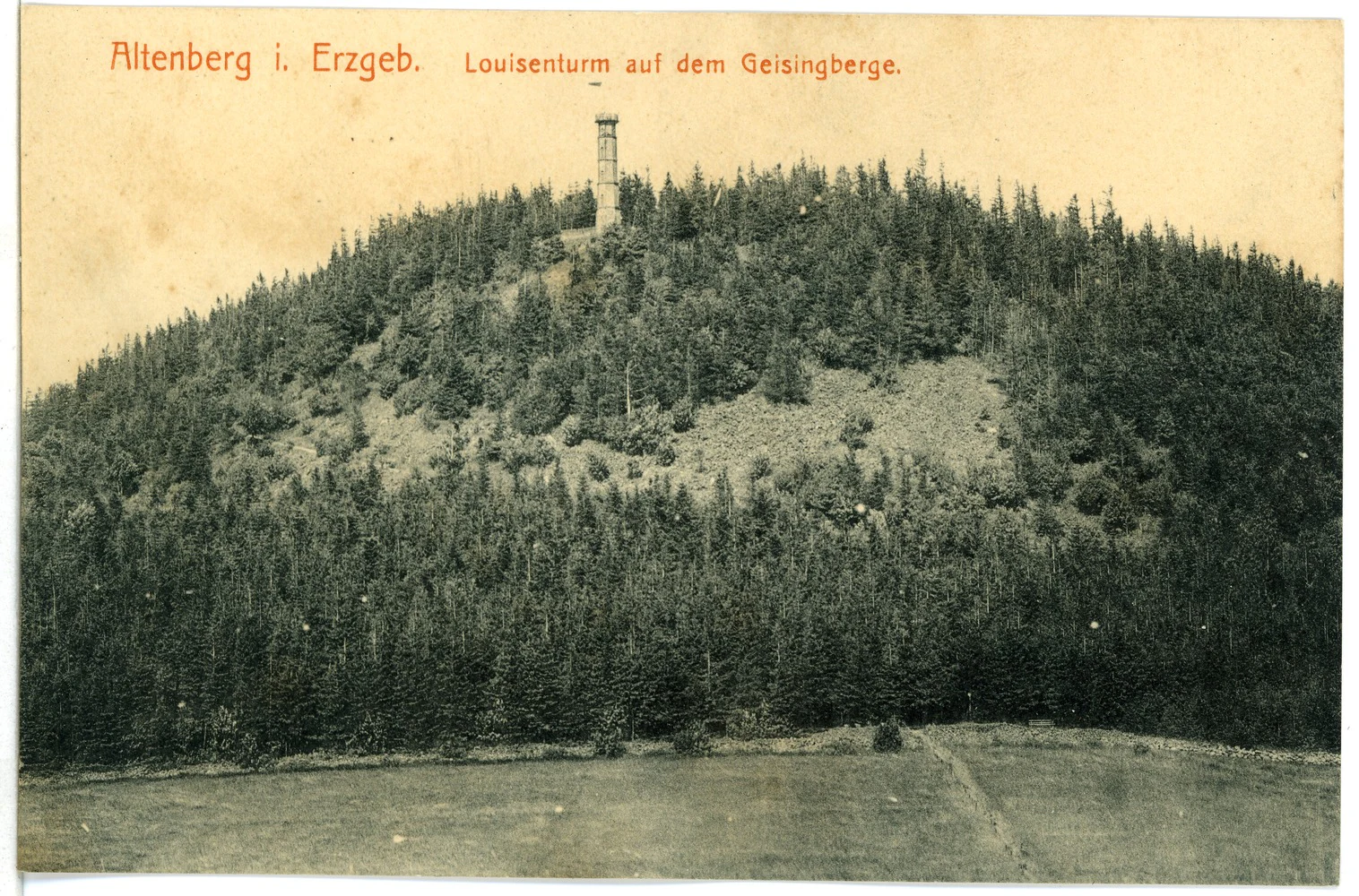 A historical, sepia-toned postcard view of a conical, forested mountain with a tall, thin observation tower situated at the summit, viewed from an open field below.