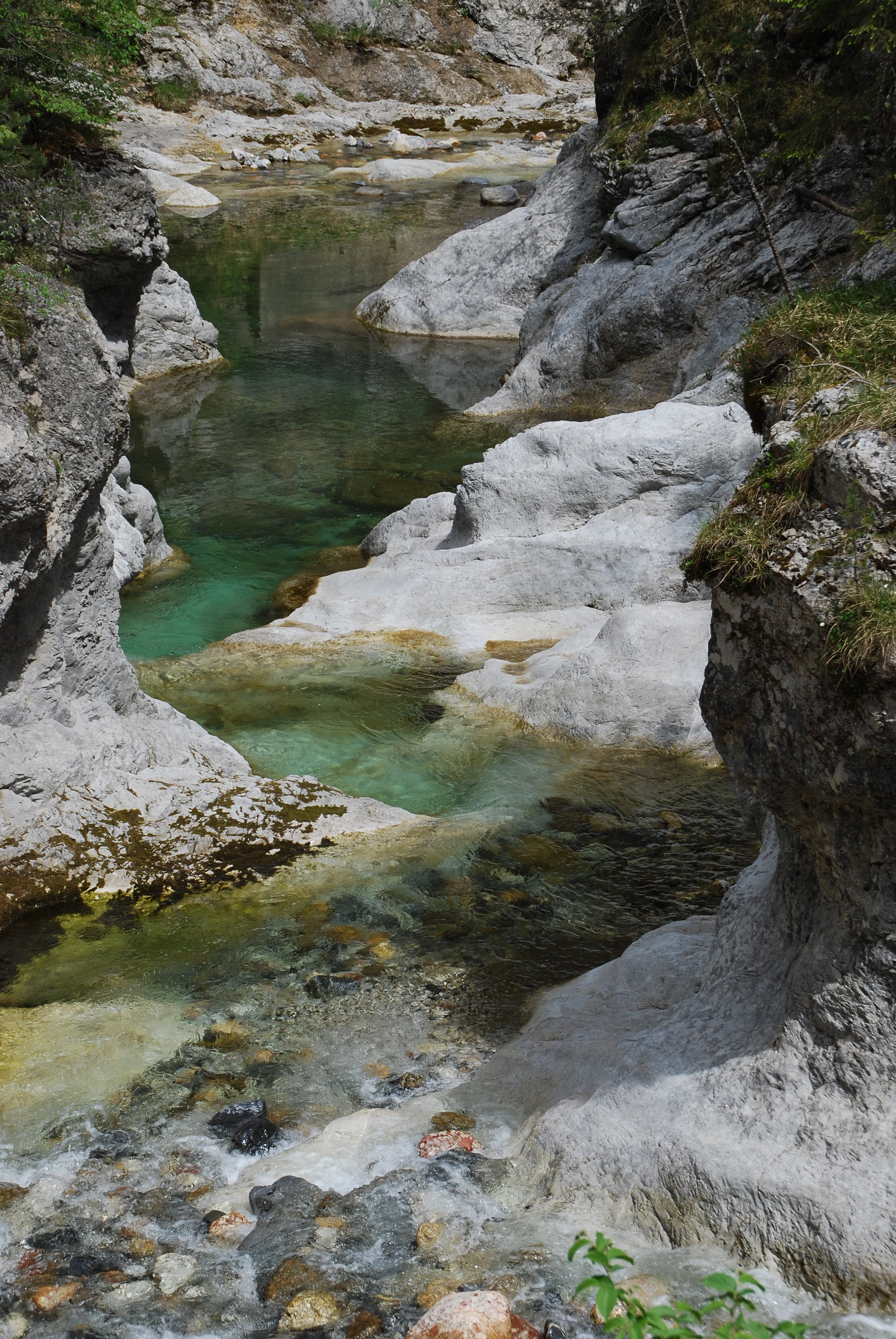 Una vista en ángulo alto de un pequeño río cristalino que fluye sobre formaciones rocosas de piedra caliza gris en un entorno de cañón.