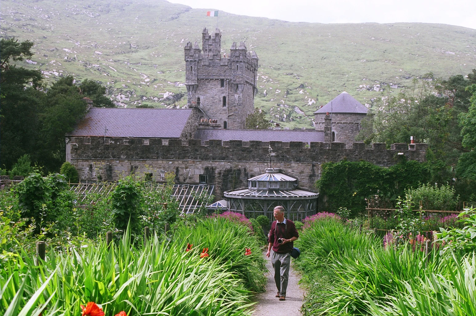 Stone castle with tower and surrounding garden pathway with a person walking