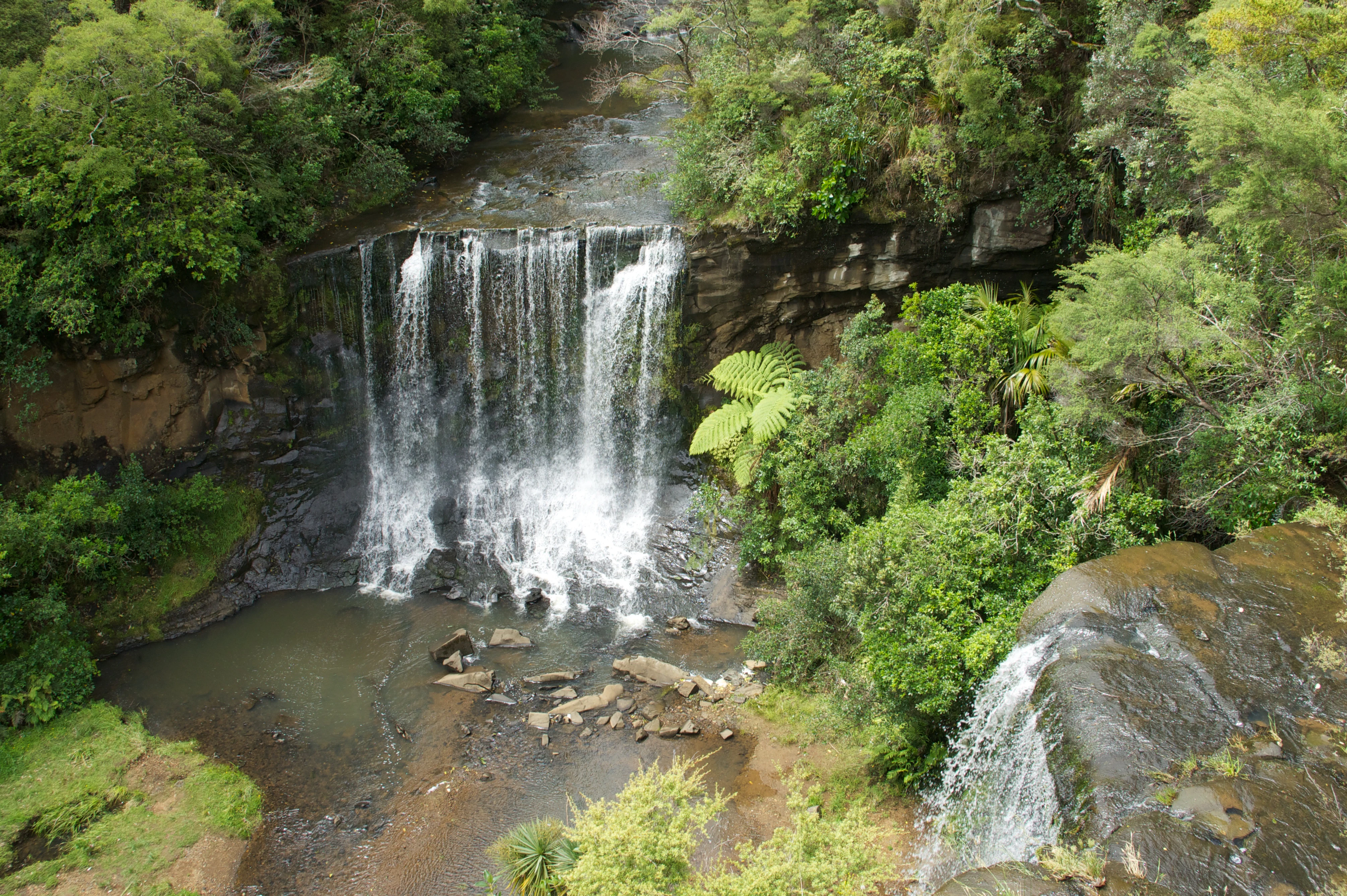 Vista en picado de una cascada de dos niveles que se precipita en una poza rocosa, rodeada de denso bosque lluvioso templado.