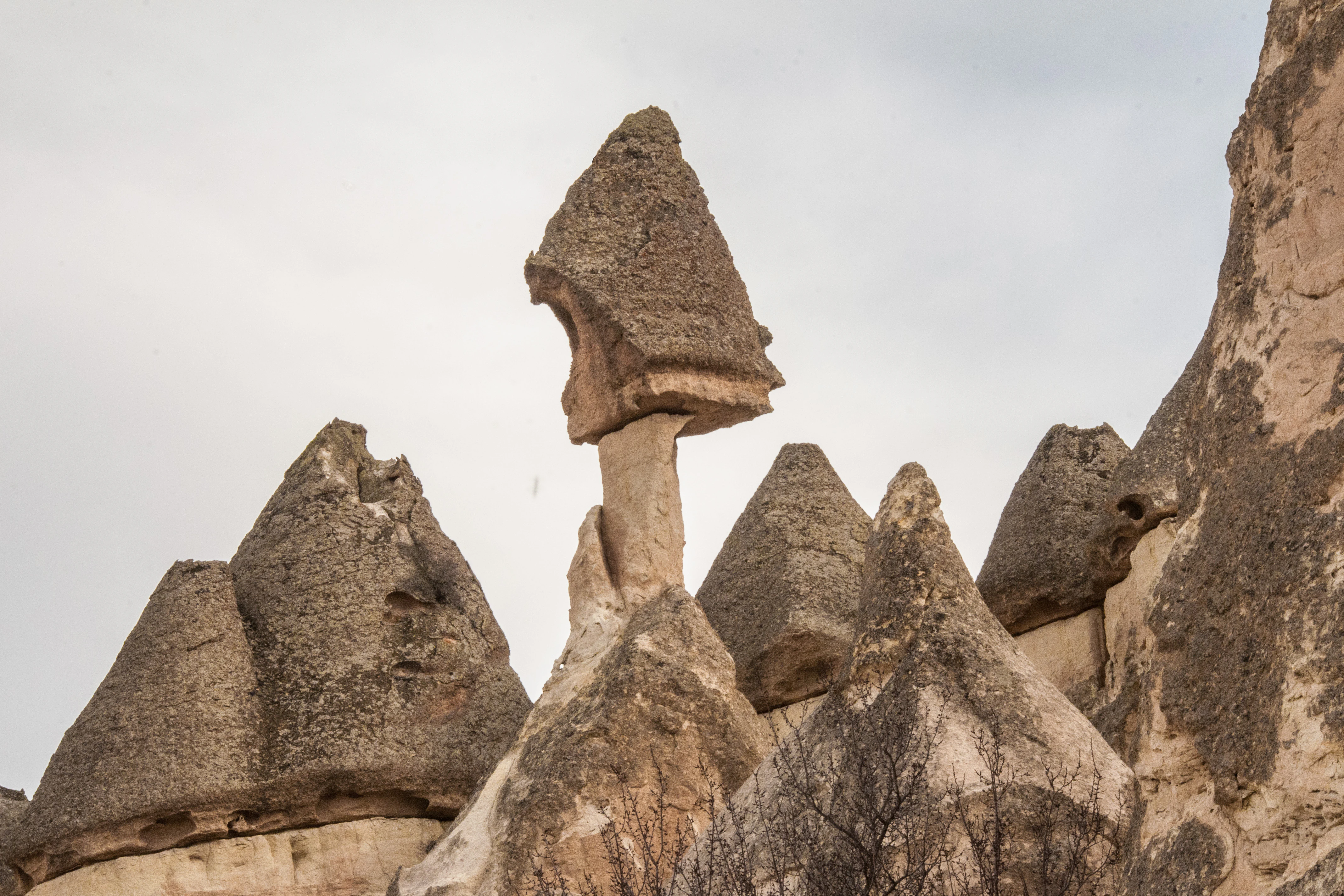 Rock formations with cone-shaped tops and flat stone caps under an overcast sky