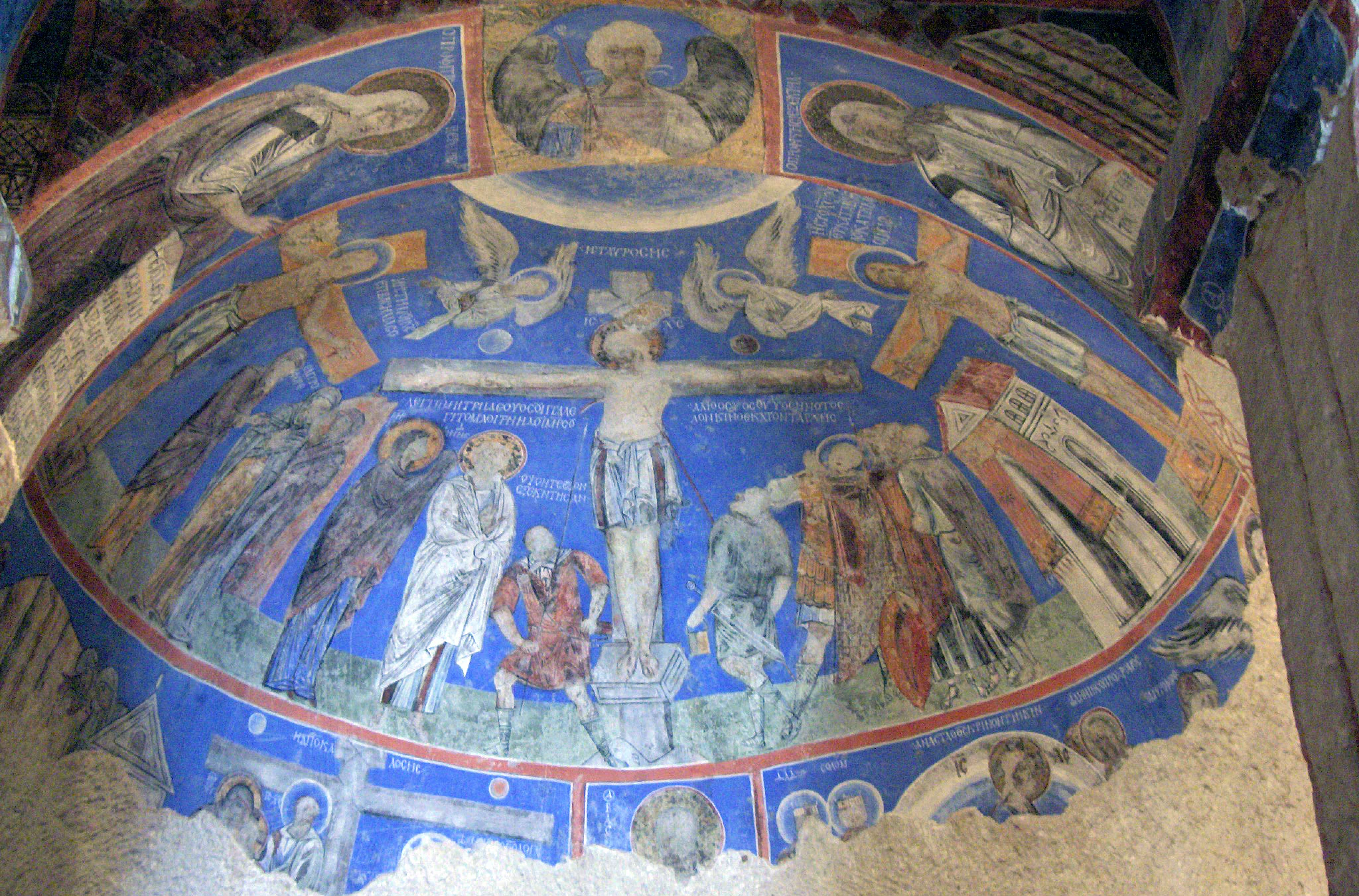 Blue fresco depicting Crucifixion scene with Jesus on cross, angels, and religious figures in circular ceiling of Tokali Church