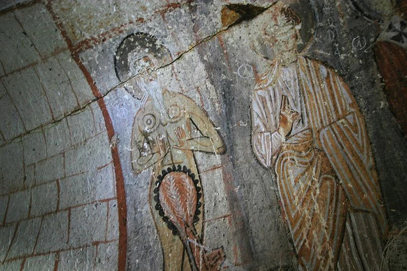 Ancient fresco depicting two religious figures on a stone wall within a cave church.