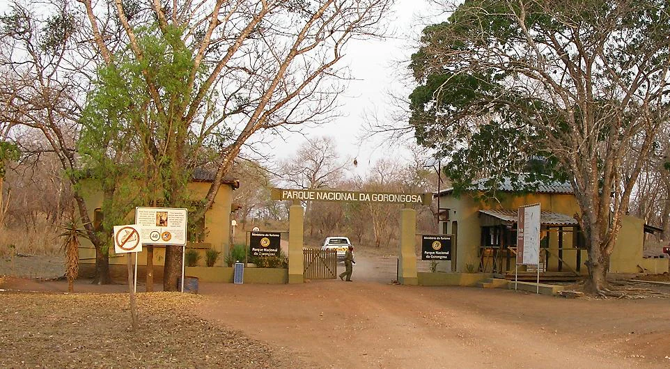 Dirt road leading to yellow building entrance with 'PARQUE NACIONAL DA GORONGOSA' sign and parked vehicle