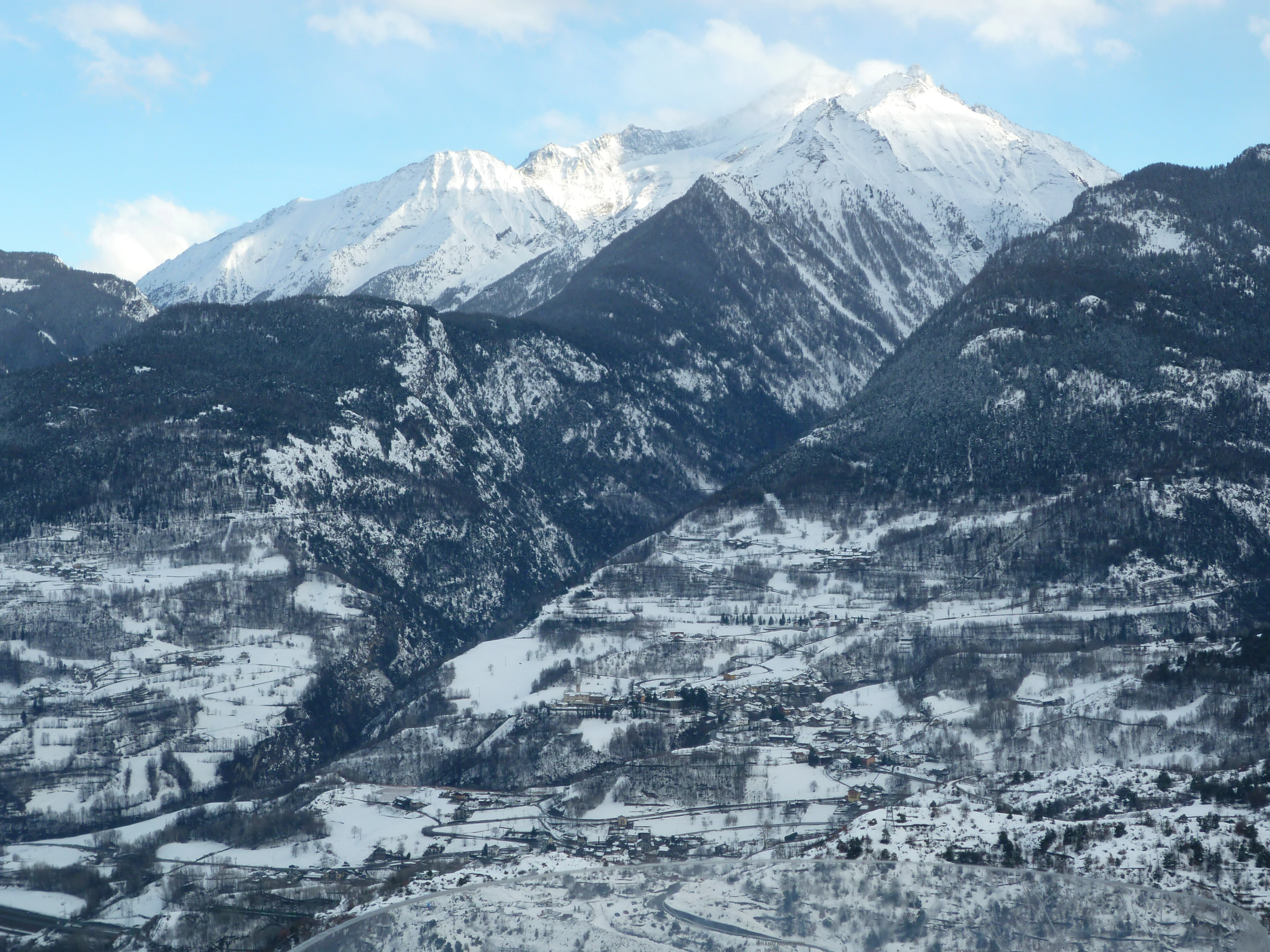 Snow-covered mountain peaks and valleys with scattered settlements in a rugged alpine landscape