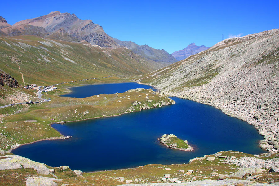 Blue alpine lake surrounded by rocky mountain slopes and grassy terrain under a clear blue sky