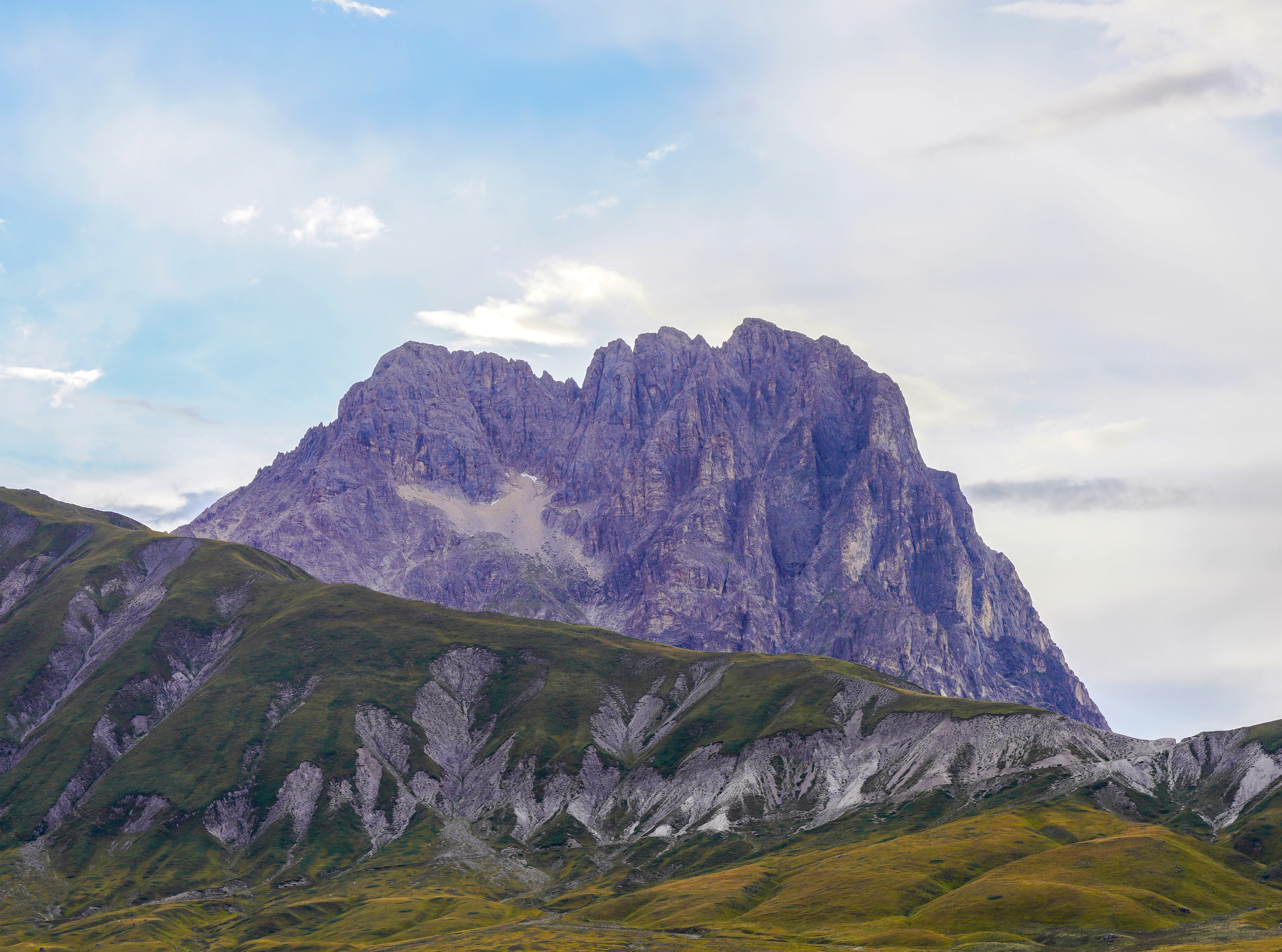 Rugged mountain peak with rocky cliffs and green slopes under a partly cloudy sky
