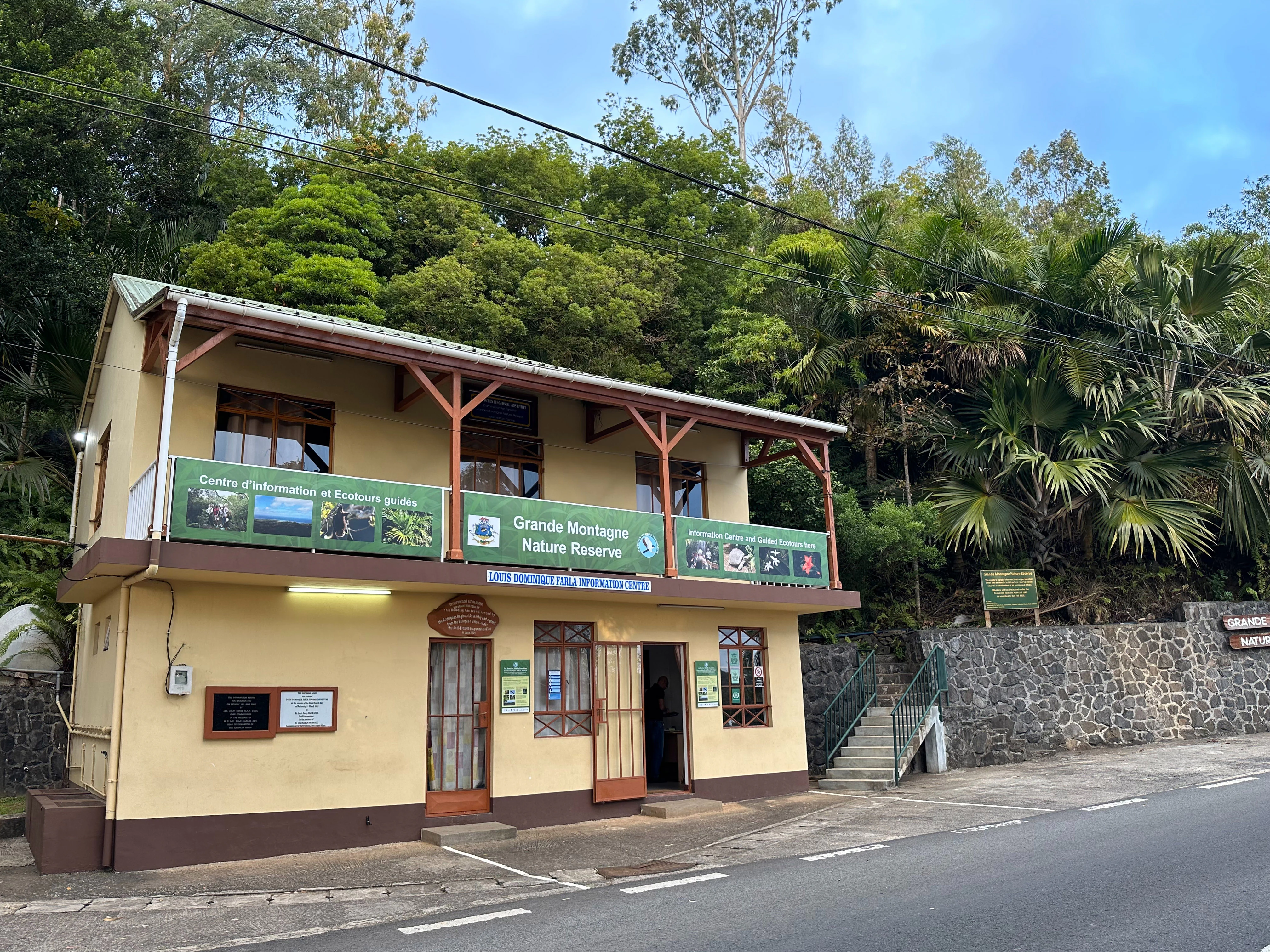 Un edificio colonial amarillo de dos plantas que alberga el centro de visitantes y el museo de la Reserva Natural de Grande Montagne, situado al pie de una ladera boscosa.