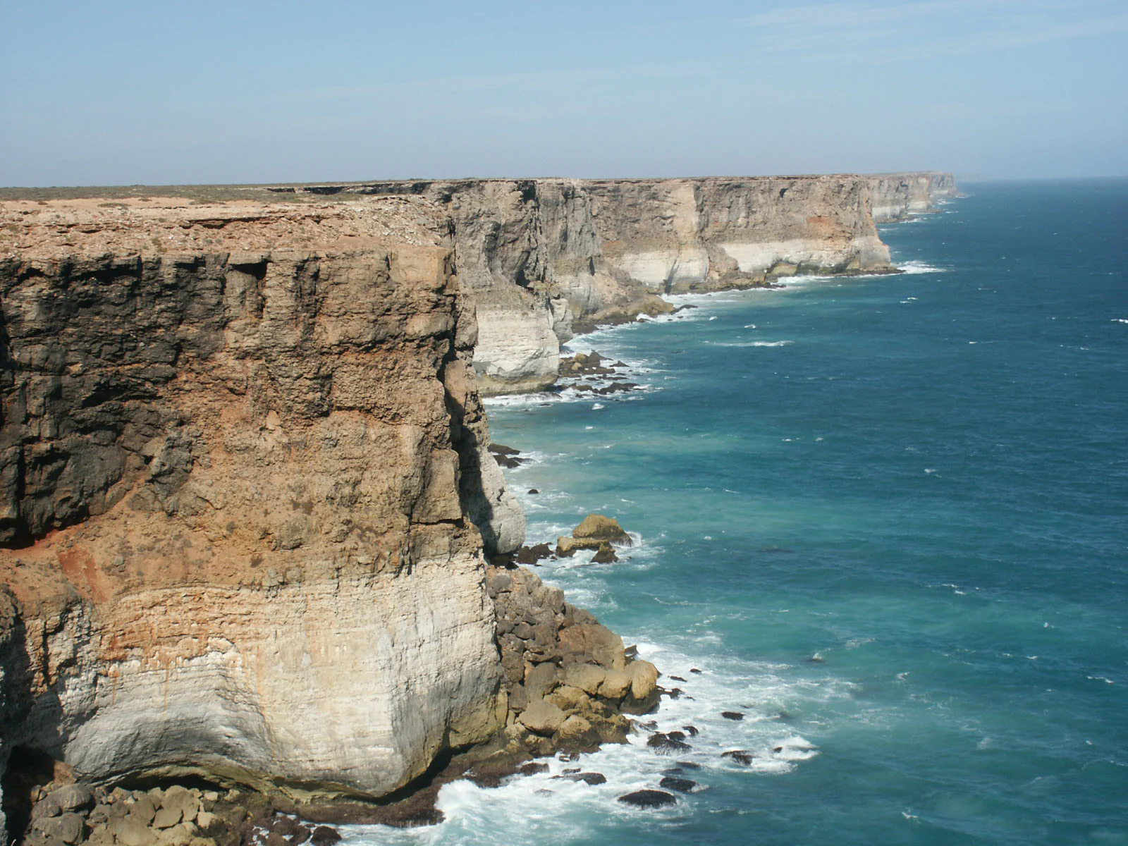 A wide angle view of the rugged, steep Bunda Cliffs dropping into the turquoise water of the ocean, with the coastline stretching into the distance.