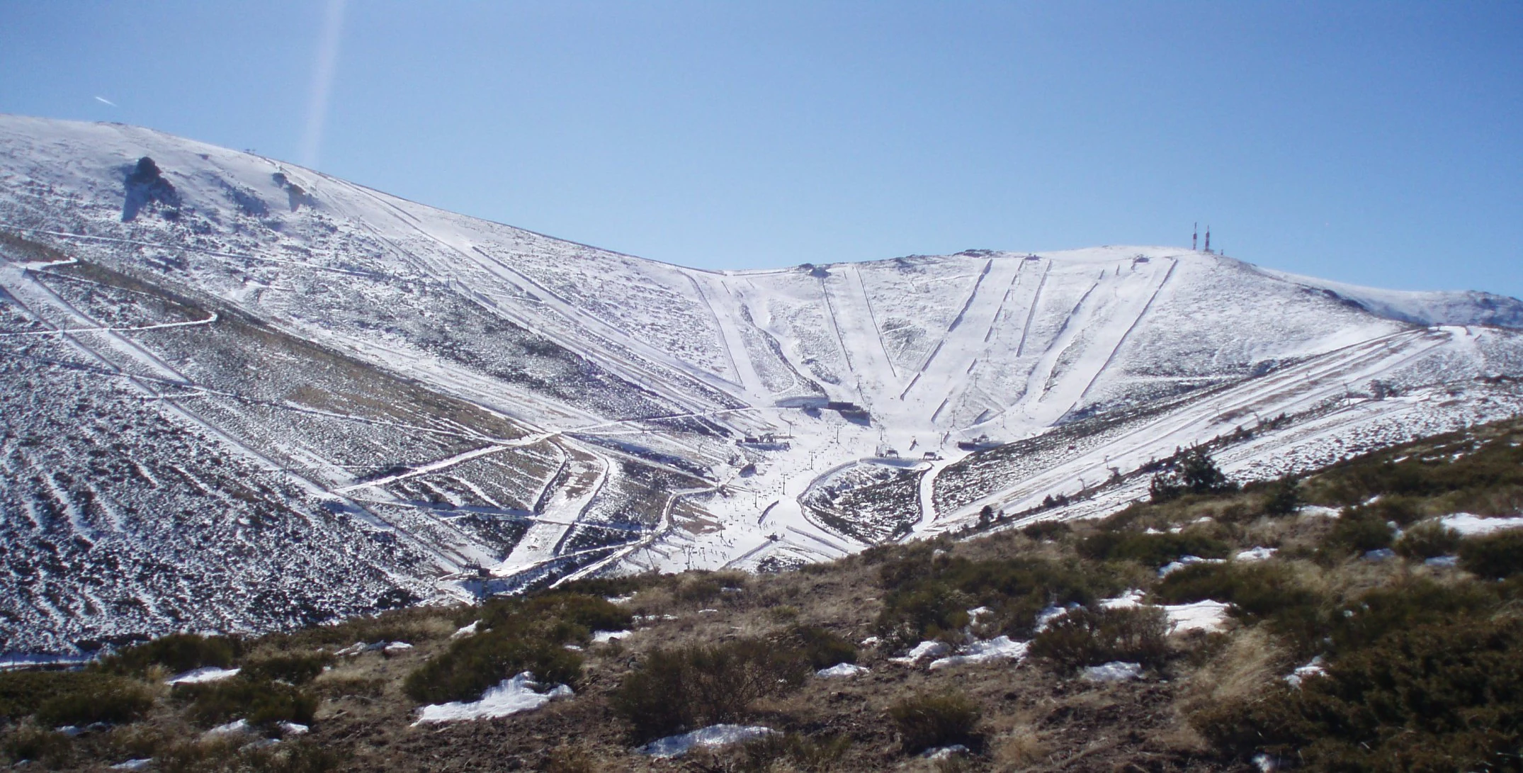 Snow-covered mountain slopes with ski trails and a distant peak under a clear blue sky