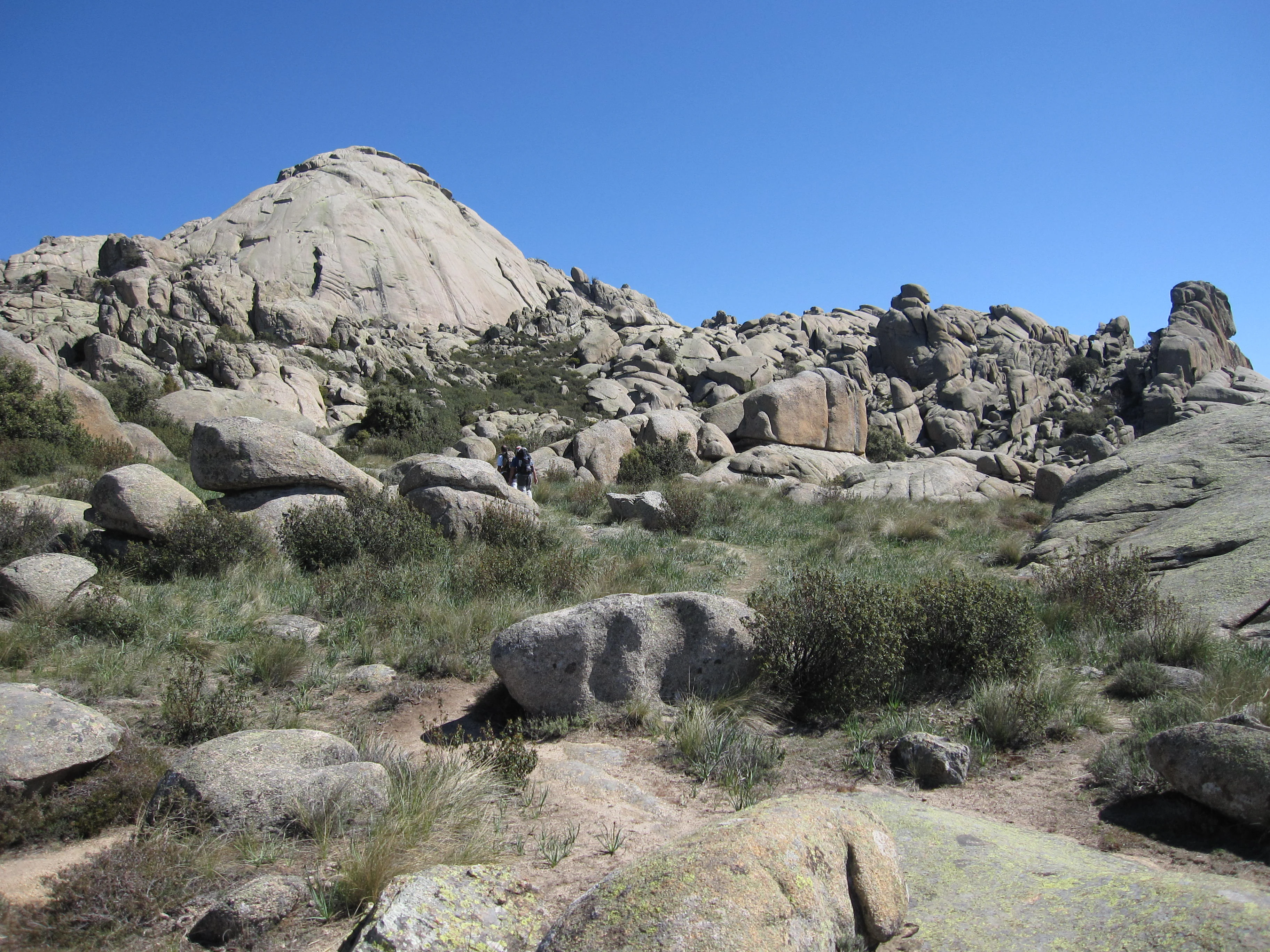 Rugged rocky landscape with large boulders and sparse vegetation under clear blue sky