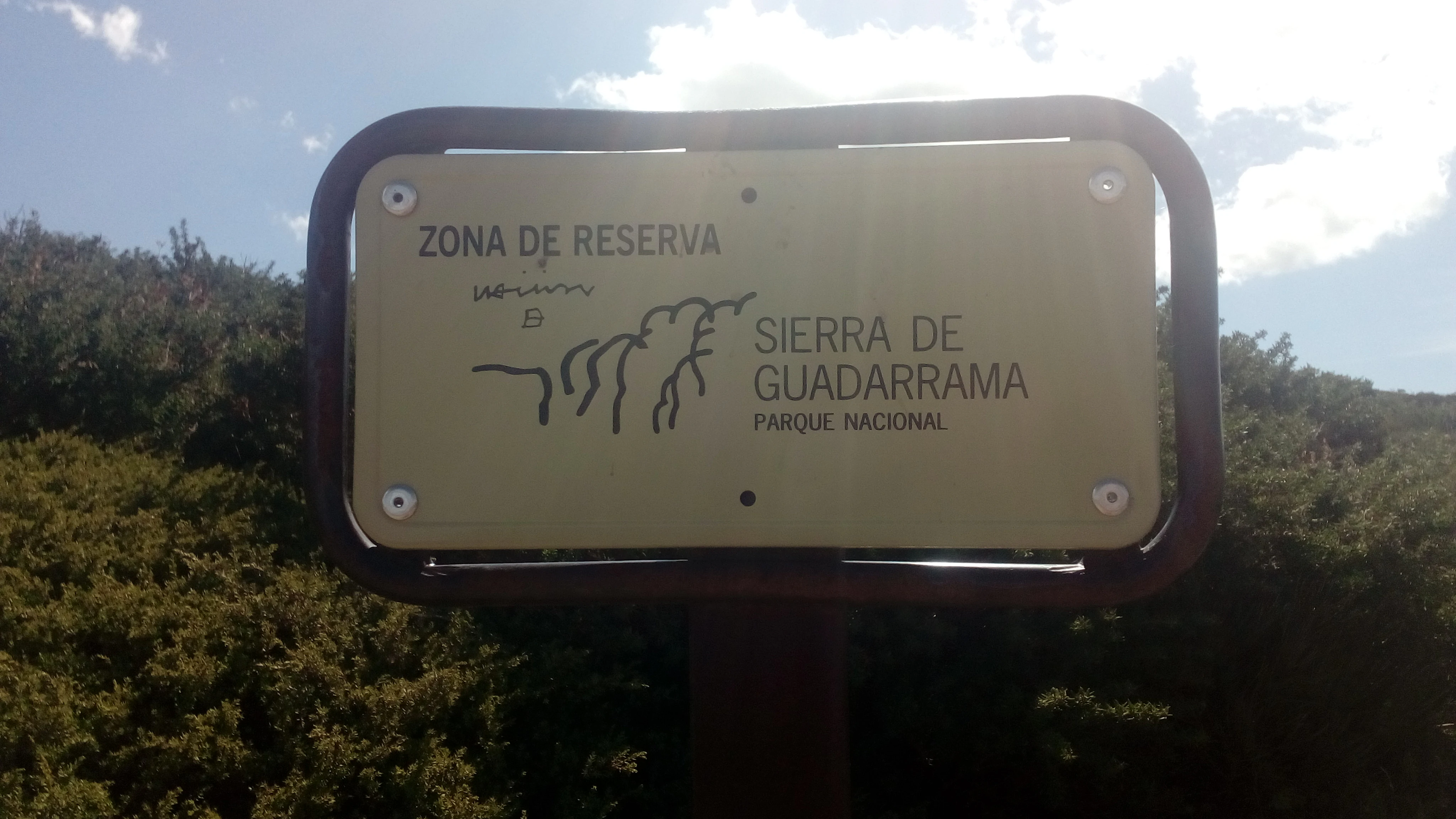 Yellow sign with dark border displaying 'Zona de Reserva' text and 'Sierra de Guadarrama Parque Nacional' with a mountain range illustration