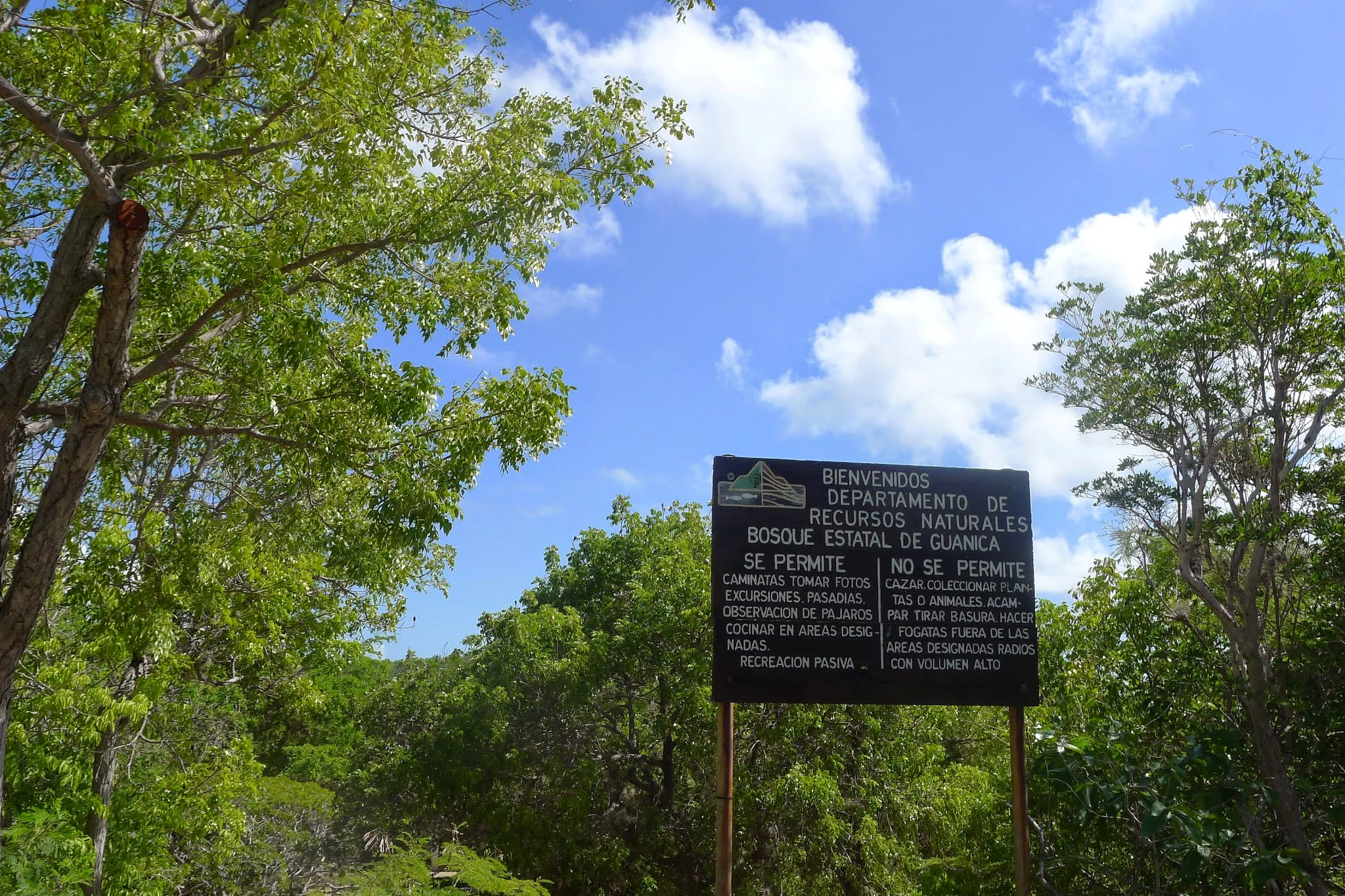 A black information sign standing in a lush green forest, detailing rules for visitors at the Guánica State Forest in Puerto Rico.