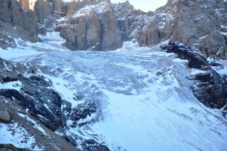 A large glacier surrounded by rocky mountain peaks with patches of snow