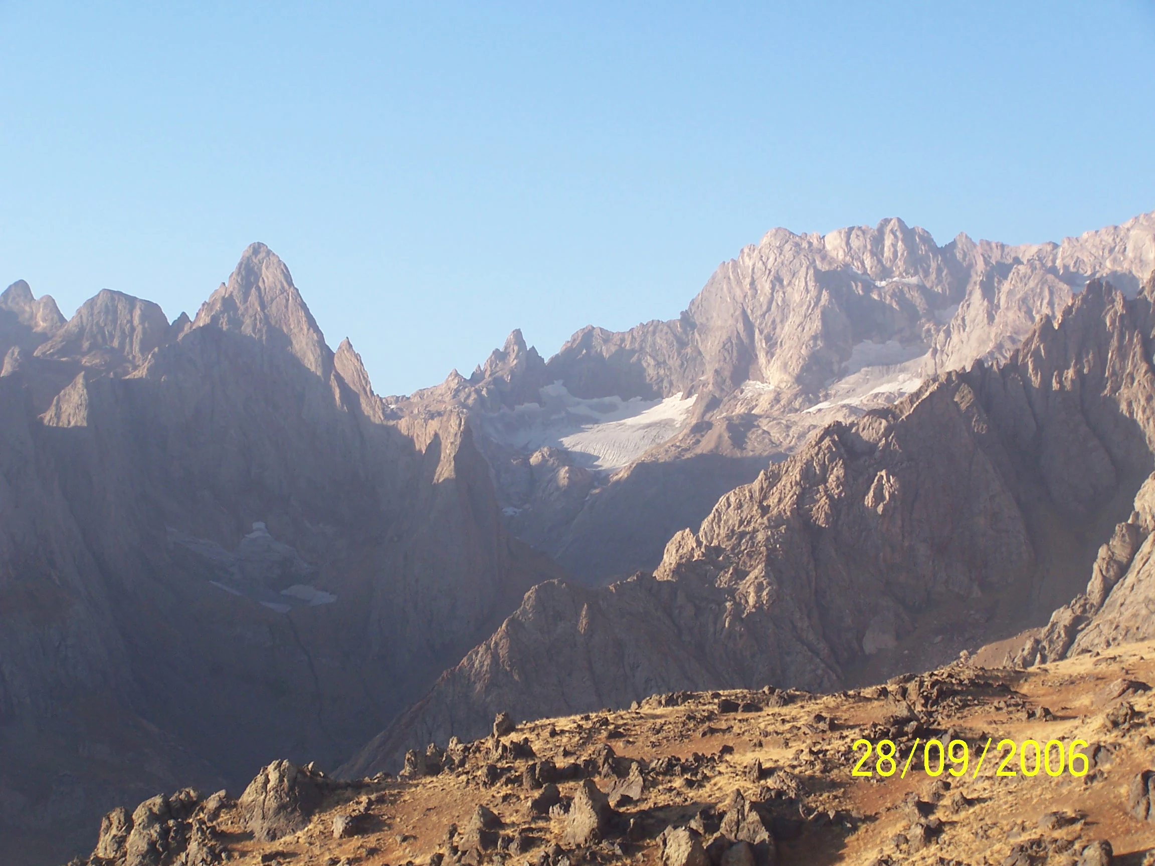 Panoramic mountain landscape showing rocky peaks with patches of snow under clear blue sky