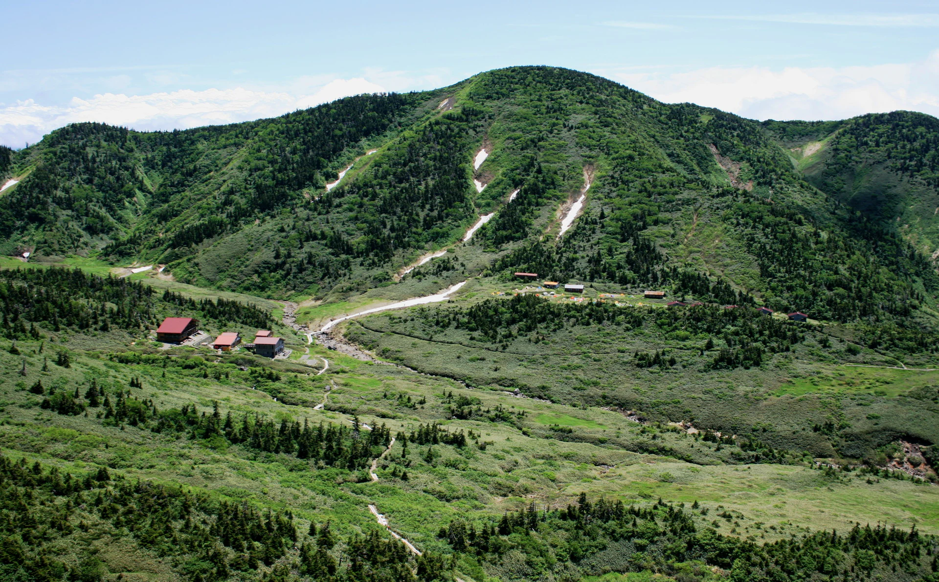 Vista amplia del monte Haku con el refugio Nanryu, montañas verdes, valles y un sendero sinuoso
