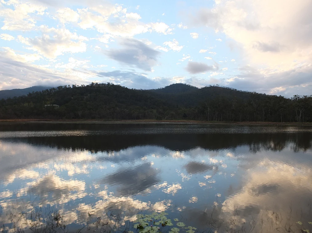 Un pantano al atardecer con agua en calma que refleja nubes y montañas boscosas
