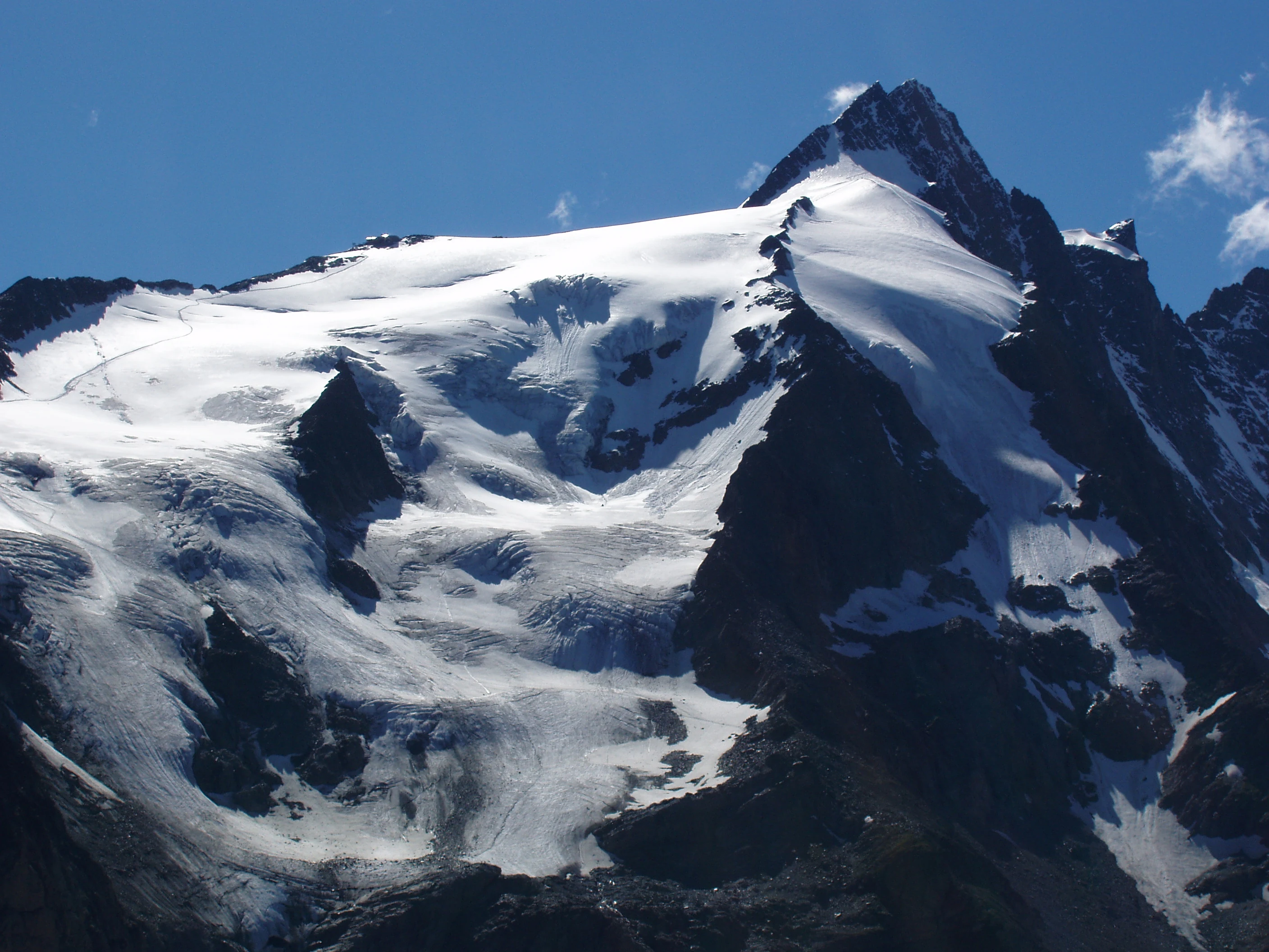 Snow-covered mountain peak with glaciers, rocky slopes, and clear blue sky