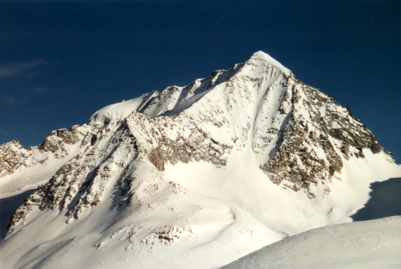 Snow-capped mountain peak with rocky outcrops under clear blue sky