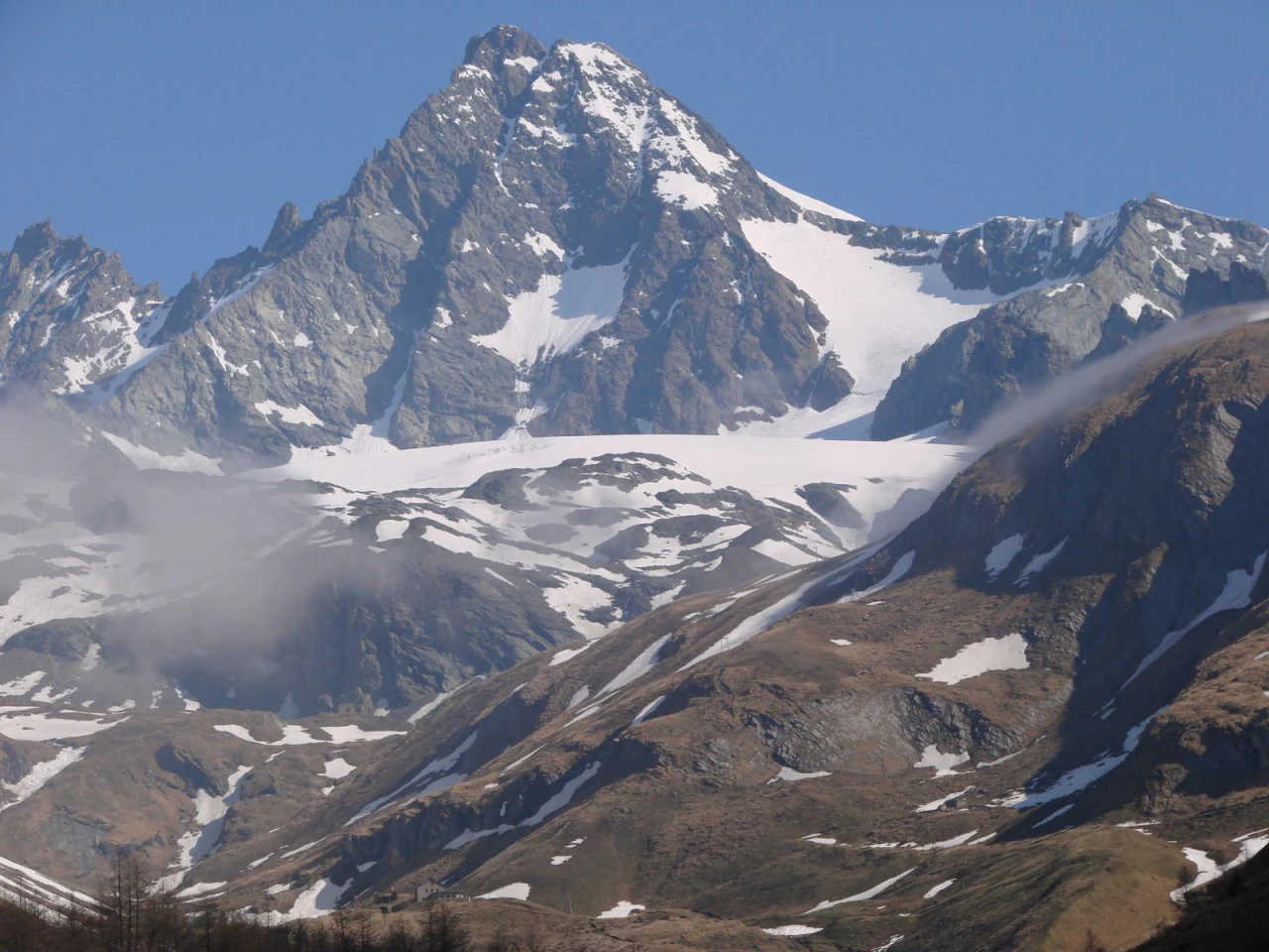 Snow-covered mountain peak with rocky slopes and visible glaciers under clear blue sky