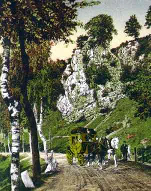 Una fotografía histórica coloreada que muestra un carruaje de caballos en un camino de tierra dentro de un valle, con formaciones rocosas de piedra caliza y árboles verdes en el fondo.