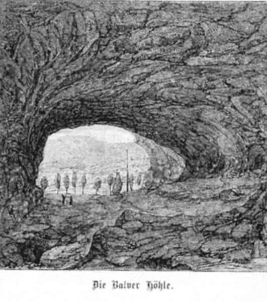Grabado histórico en blanco y negro que muestra el interior rocoso de una gran cueva, mirando hacia el exterior a través de una amplia entrada arqueada hacia árboles y pequeñas figuras en la distancia, con el texto 'Die Balver Höhle.' en la parte inferior.