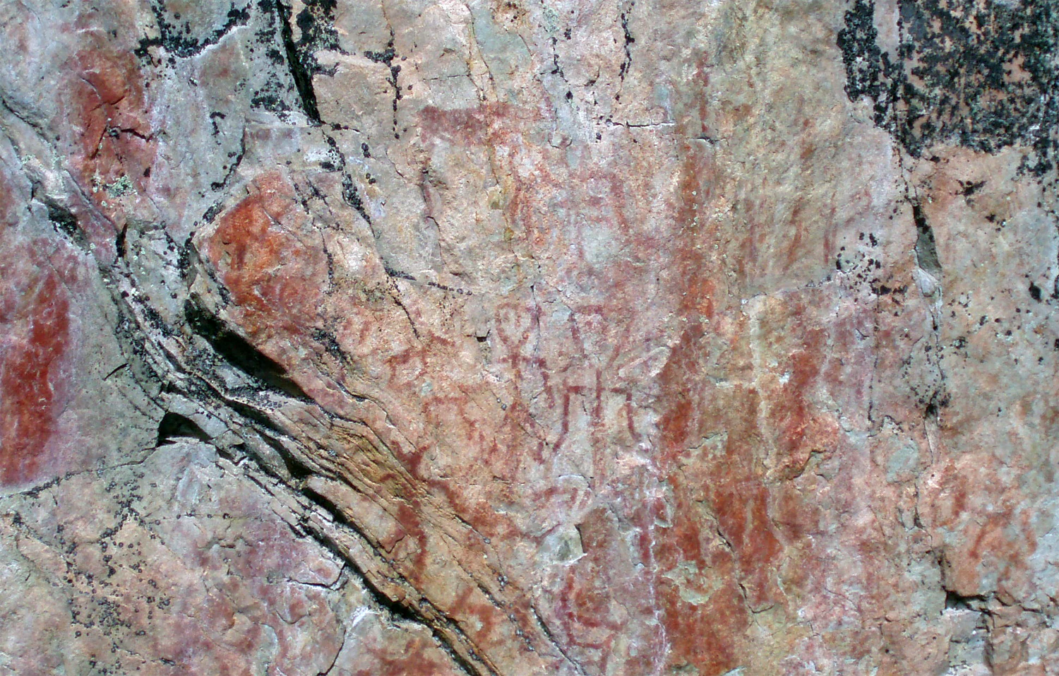 Prehistoric rock painting on stone surface with red and orange markings showing abstract patterns and figures