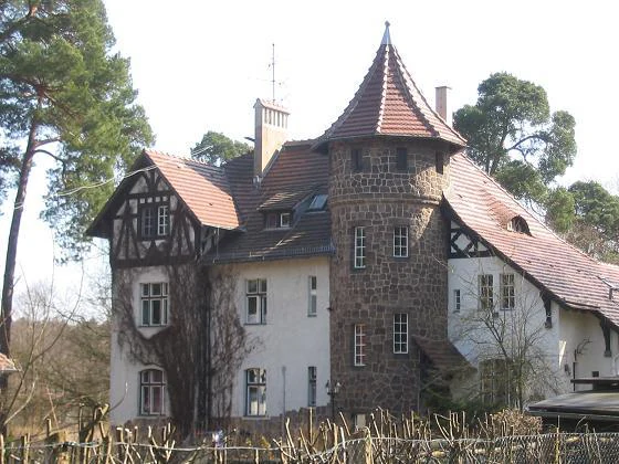 A historic, multi-story forest house with a stone tower and timber-framed elements, situated within a wooded area.
