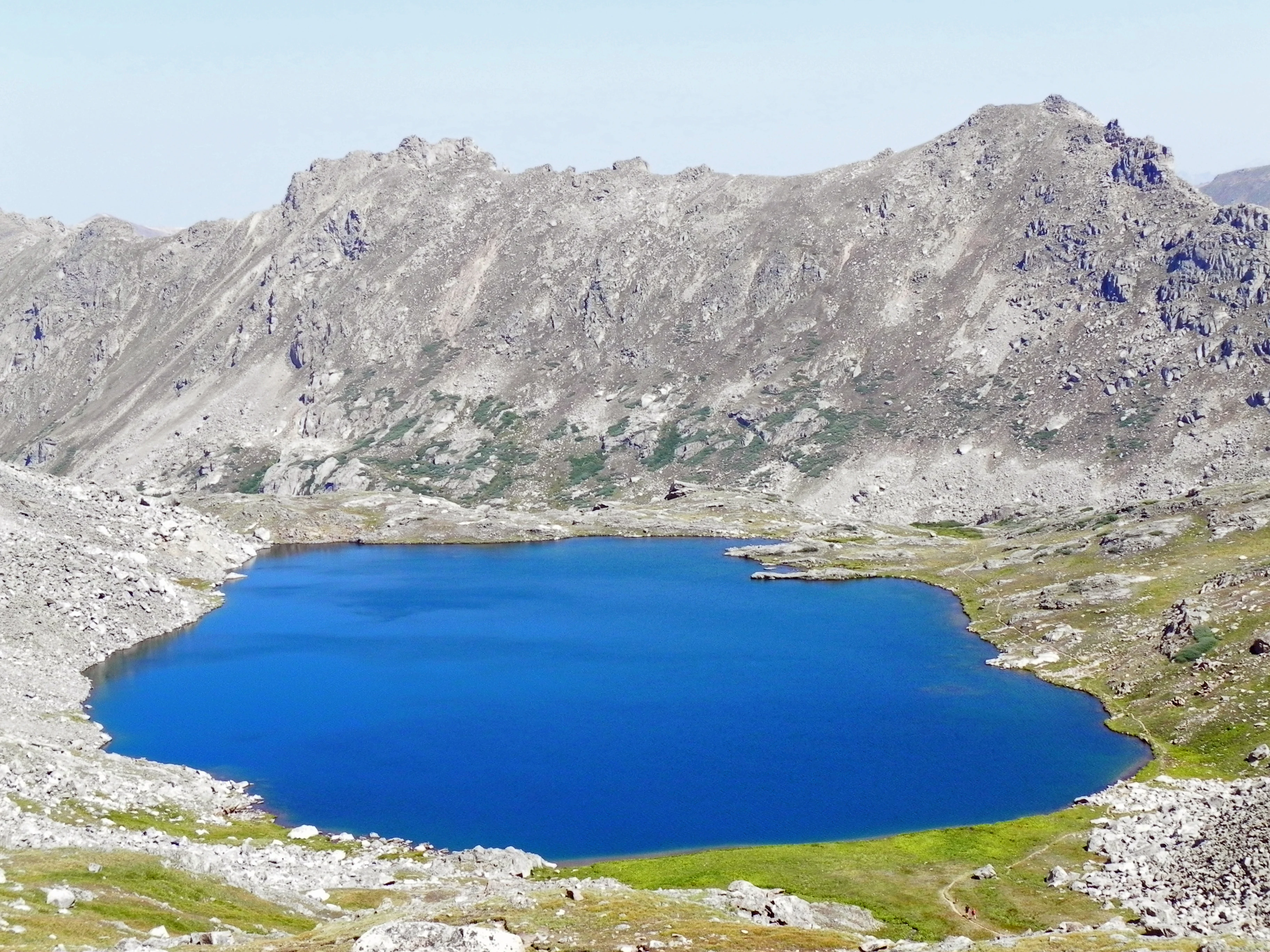 A deep blue alpine lake surrounded by steep, rocky mountain slopes under a clear sky.