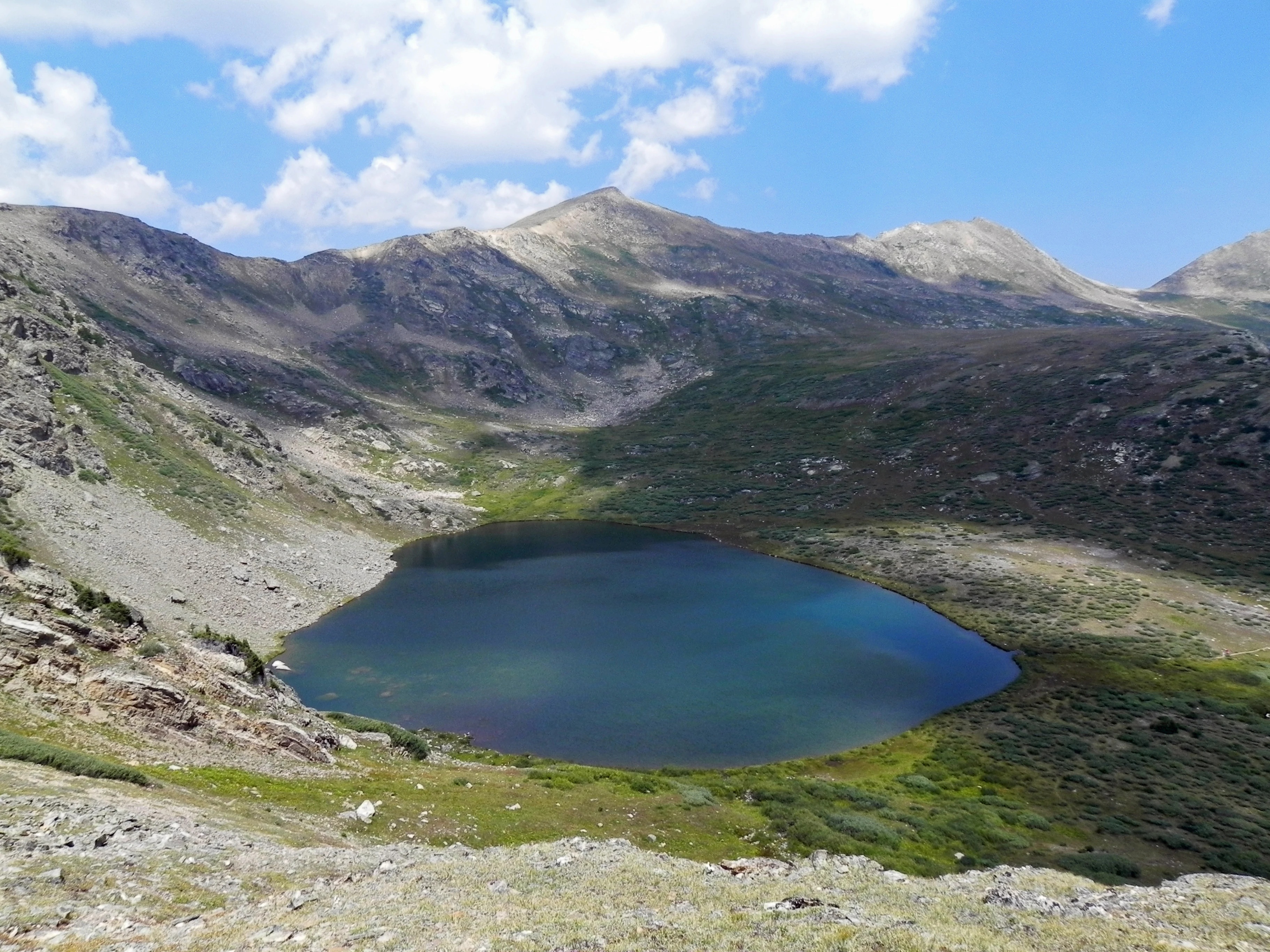 A high-altitude alpine lake surrounded by rocky slopes and sparse tundra vegetation under a blue sky.