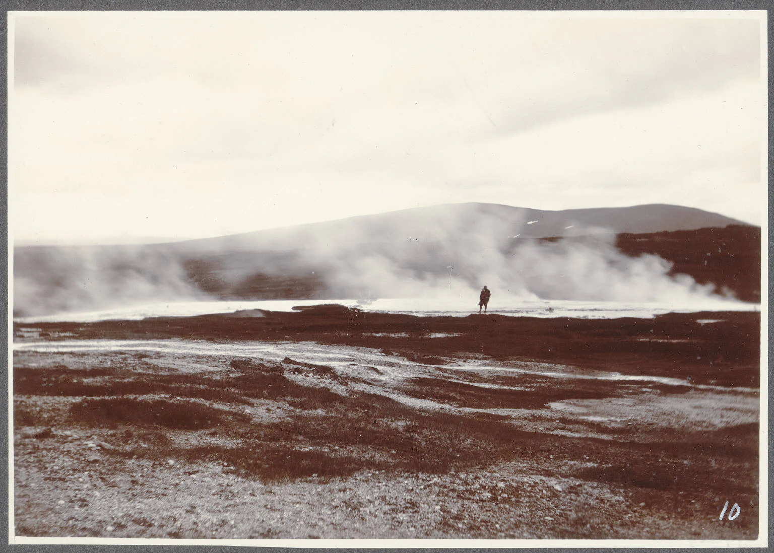 A sepia-toned vintage photograph showing a steaming geothermal area in Iceland with a lone figure standing near the vents.