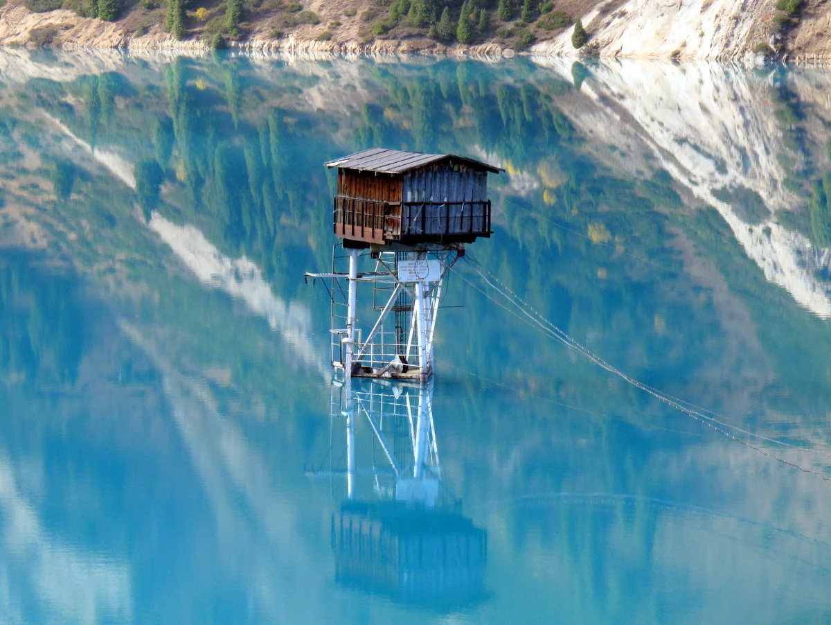 Wooden watchtower on stilts in the middle of a blue lake with surrounding mountain reflections