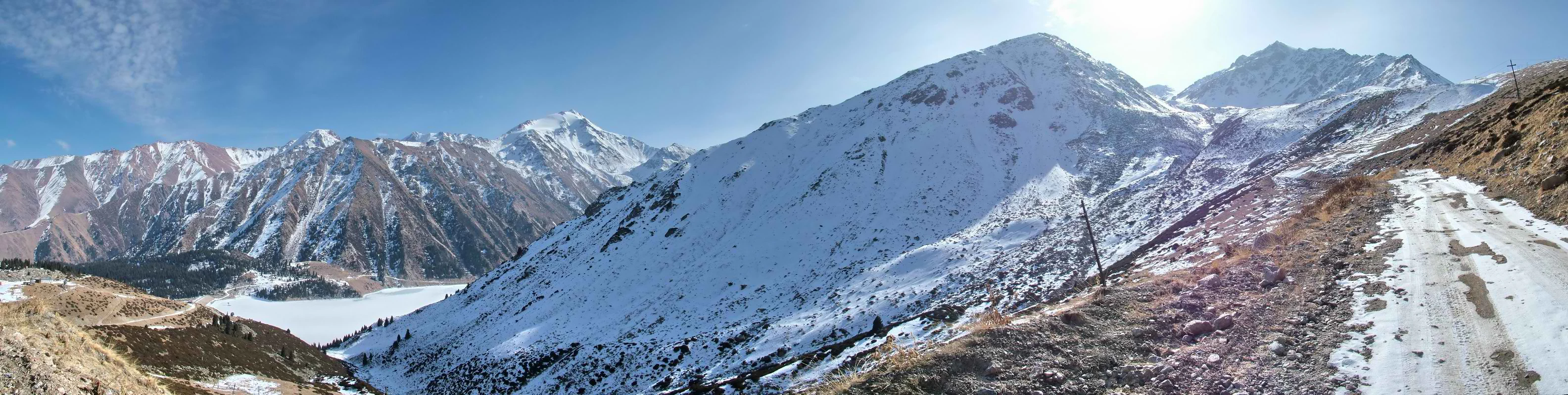 Snow-covered mountain peaks, a valley with a lake, and a dirt road in Ile-Alatau National Park