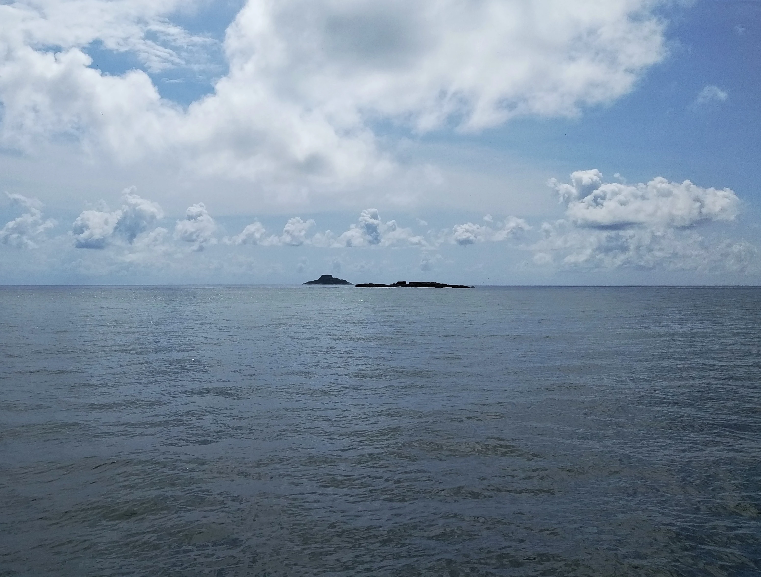 Océano tranquilo con dos pequeñas islas en el horizonte bajo un cielo parcialmente nublado