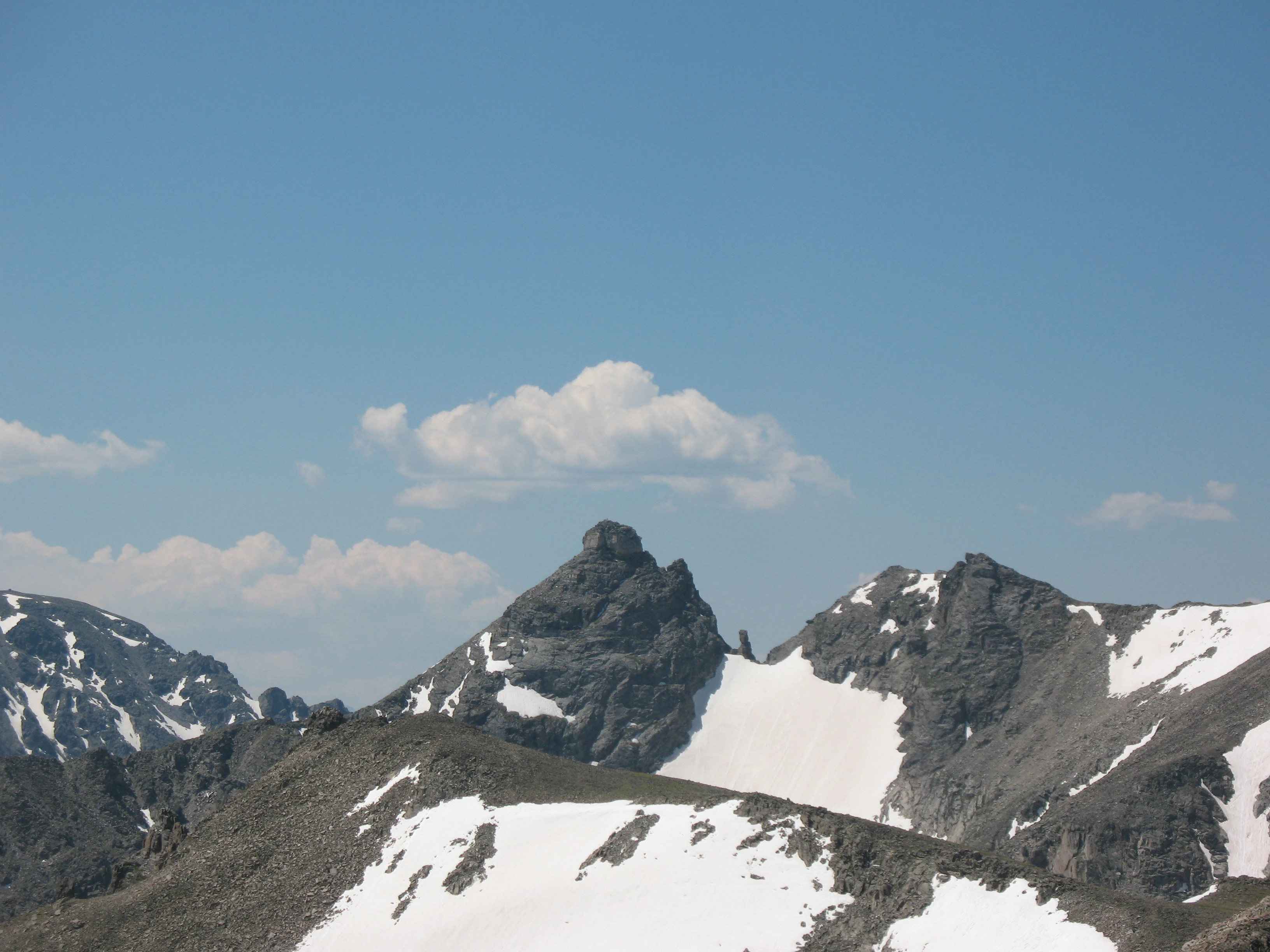Rugged, rocky mountain peaks featuring patches of snow against a clear blue sky.