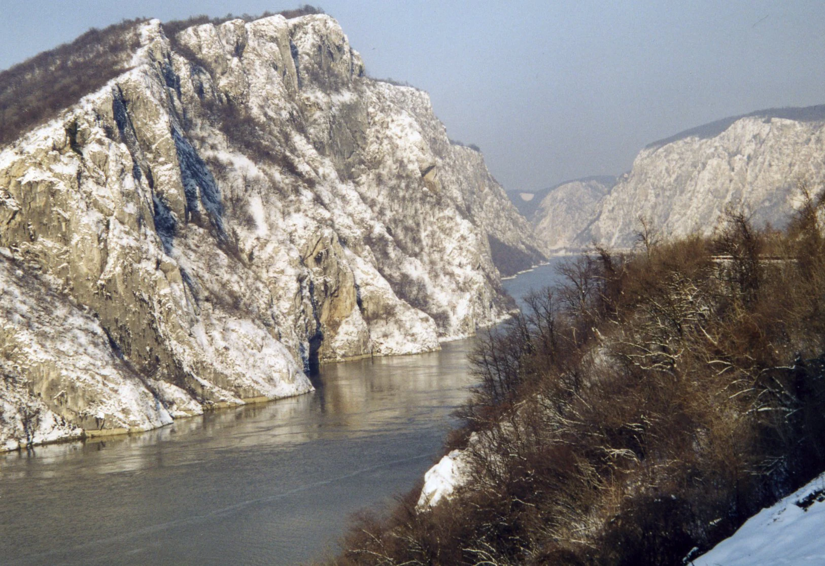 Steep rocky cliffs with patches of snow bordering the Danube River in Iron Gates Natural Park