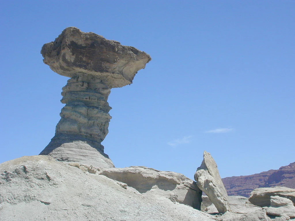 A large, mushroom-shaped sandstone rock formation stands in a desolate, arid landscape against a clear blue sky.