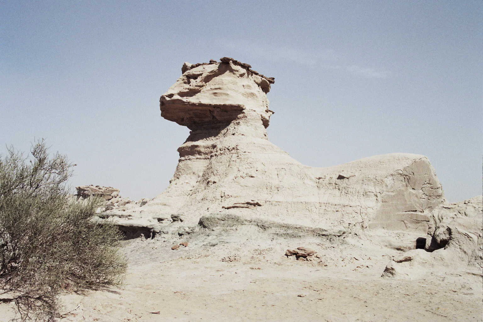 A large, weathered, light-colored rock formation known as The Sphinx, surrounded by arid, sandy terrain under a clear sky.