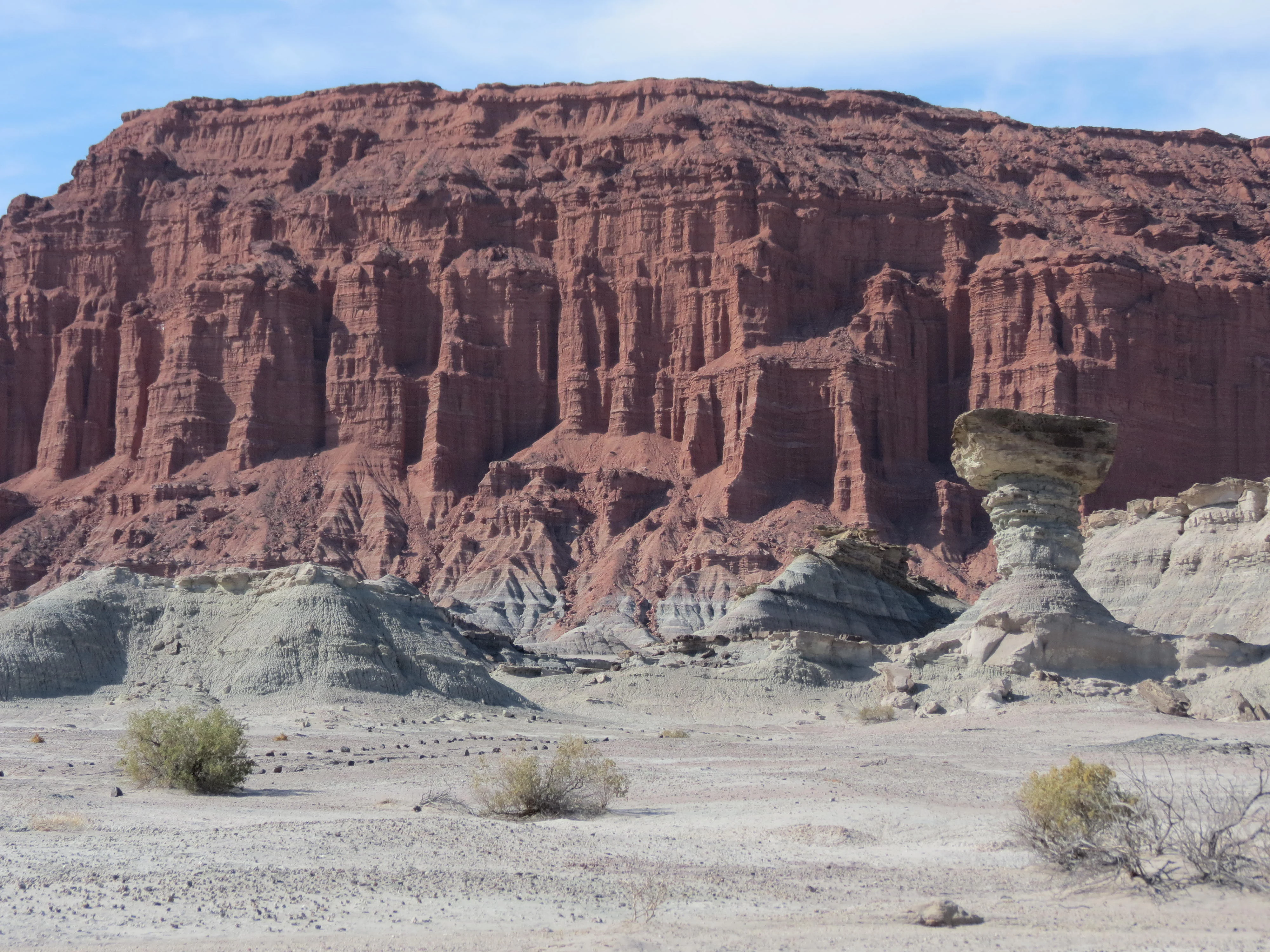A wide, eye-level shot of the iconic mushroom-shaped rock formation in the foreground, with the massive, stratified red rock cliffs of the Red Ravines in the background.