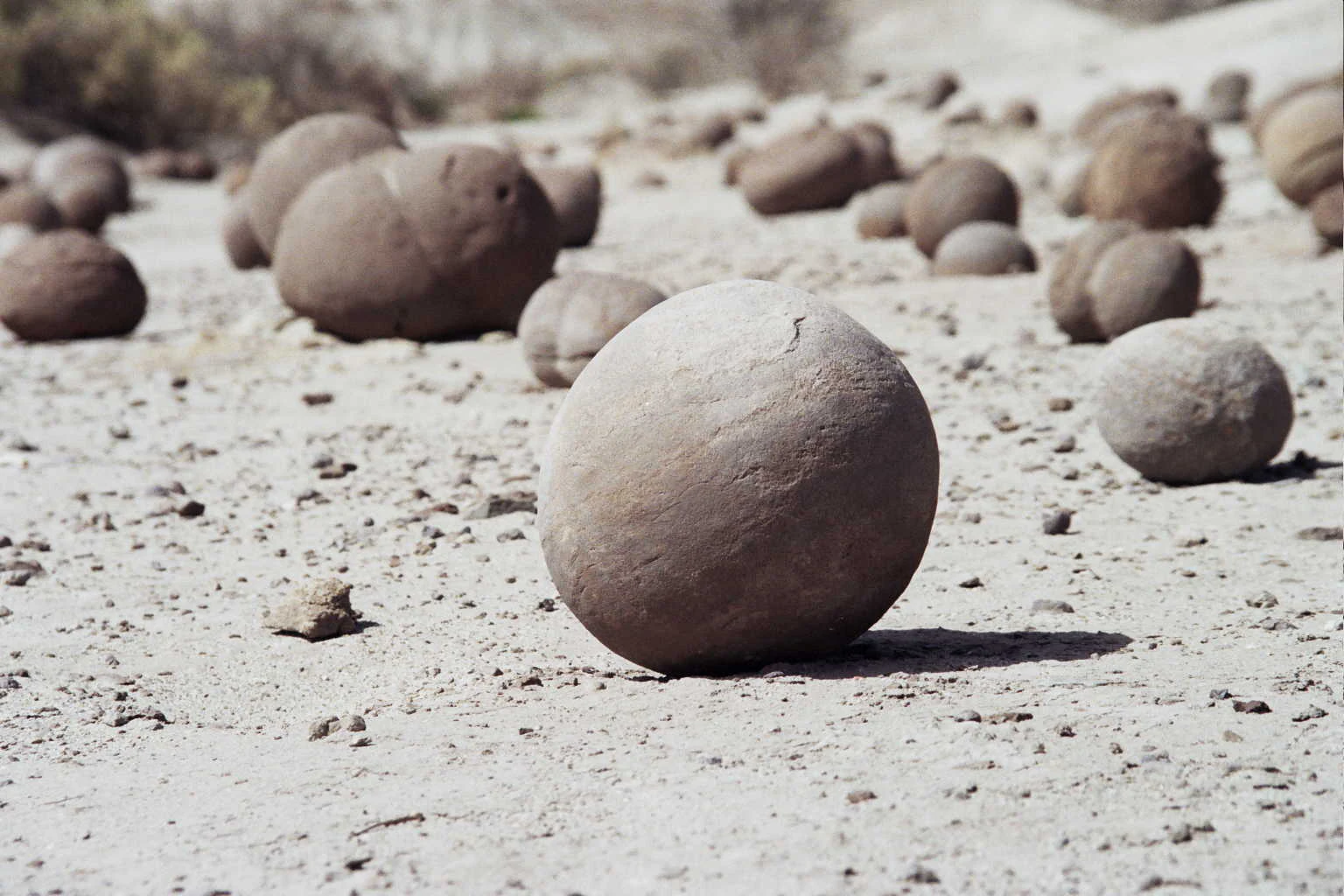 Multiple smooth, spherical rock formations resting on a flat, sandy, arid landscape under bright daylight.