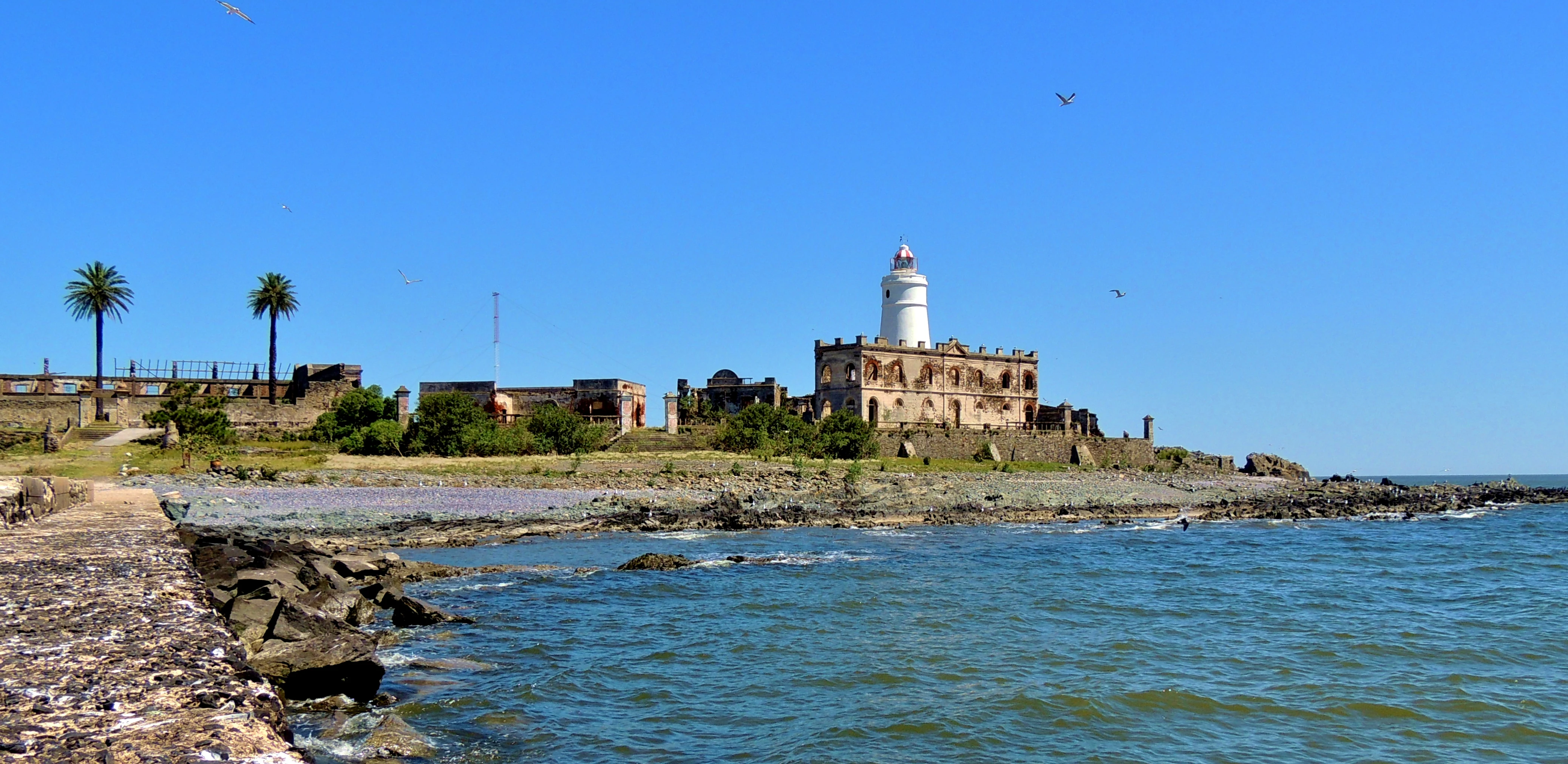 A sunny view of the historic lighthouse and stone ruins on Isla de Flores, surrounded by the Rio de la Plata.