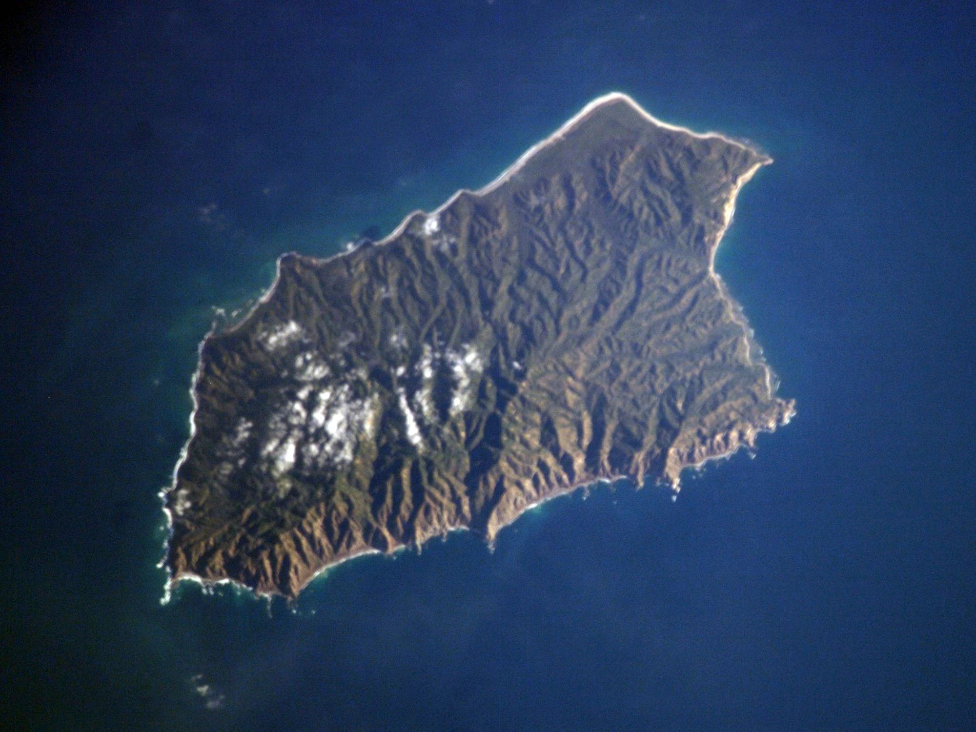 Fotografía satelital desde el espacio que muestra el terreno accidentado y verde de la isla María Magdalena, rodeada por las aguas azul profundo del océano Pacífico.
