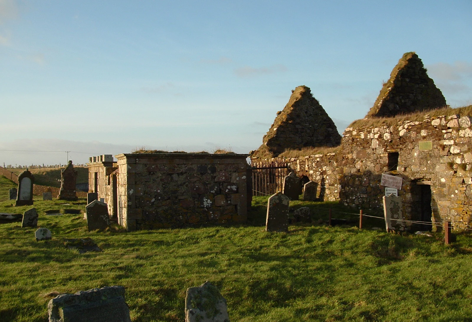 The stone ruins of an ancient church with two gabled wall segments remaining, set within a grass-covered cemetery on the Isle of Lewis.