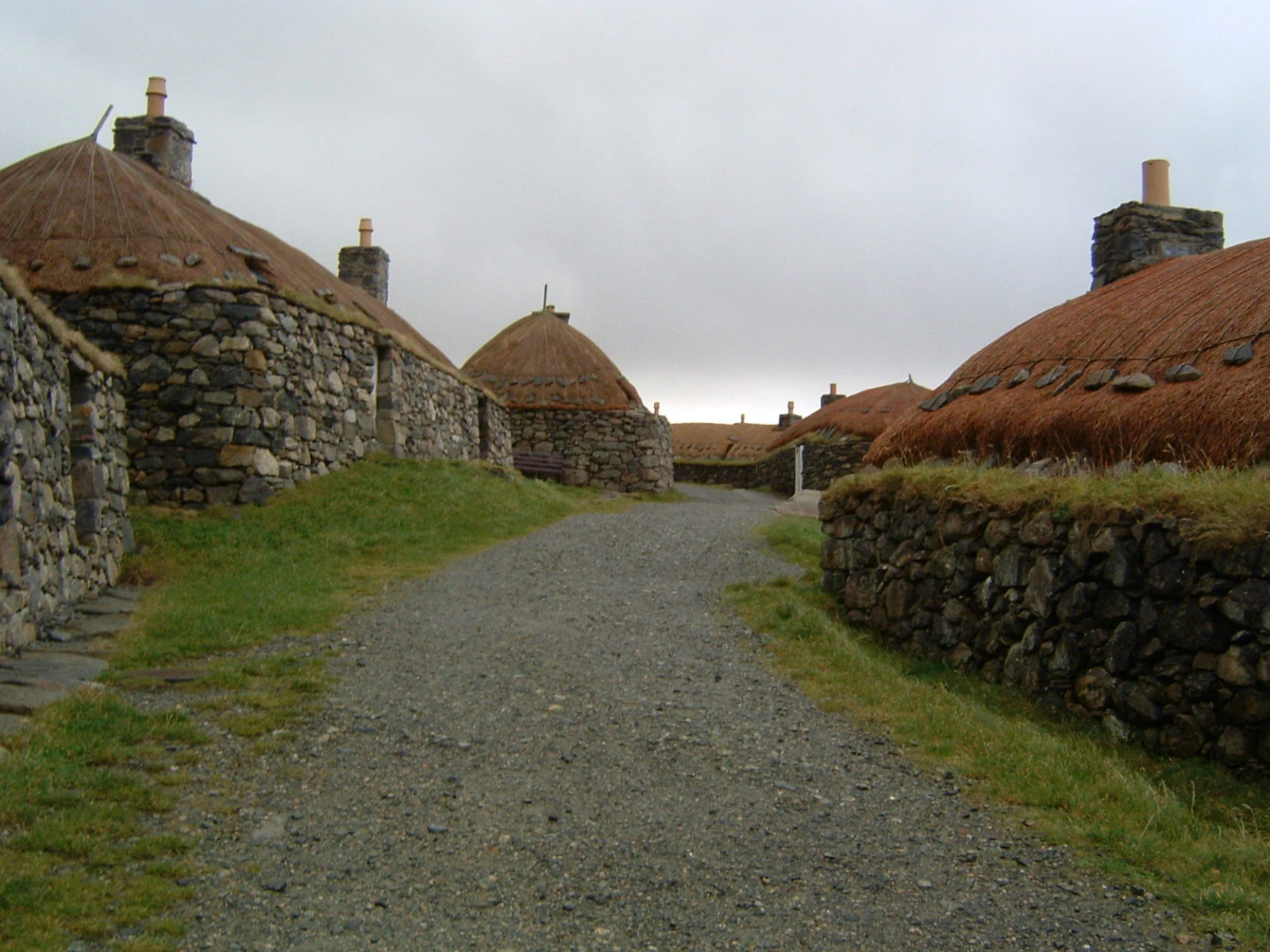 A gravel path leads through a row of traditional stone cottages with thatched roofs at the Garenin Blackhouse Village.