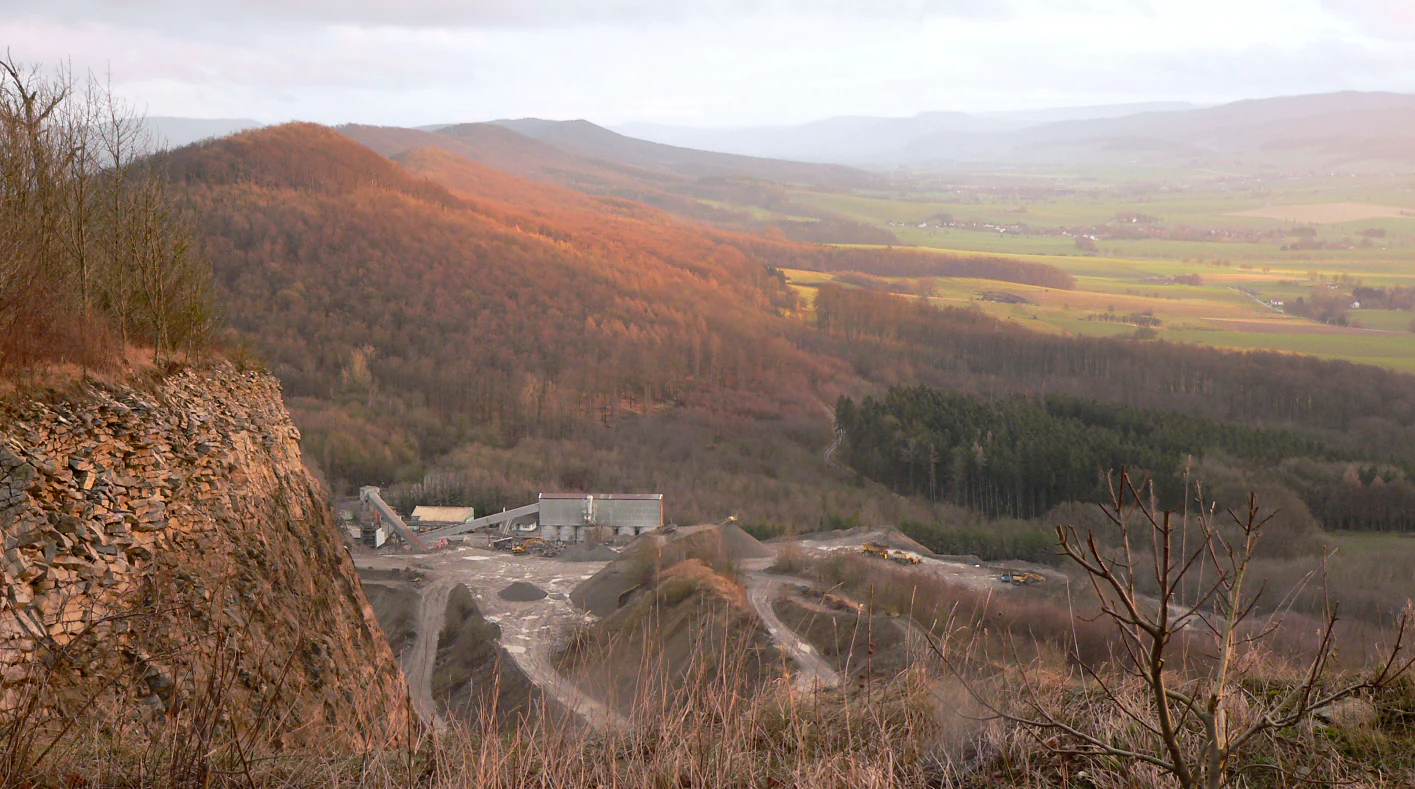 A wide angle landscape view of the Ith mountain range showing a steep rock face of a quarry in the foreground and a forested ridge sloping down into a valley in the distance.